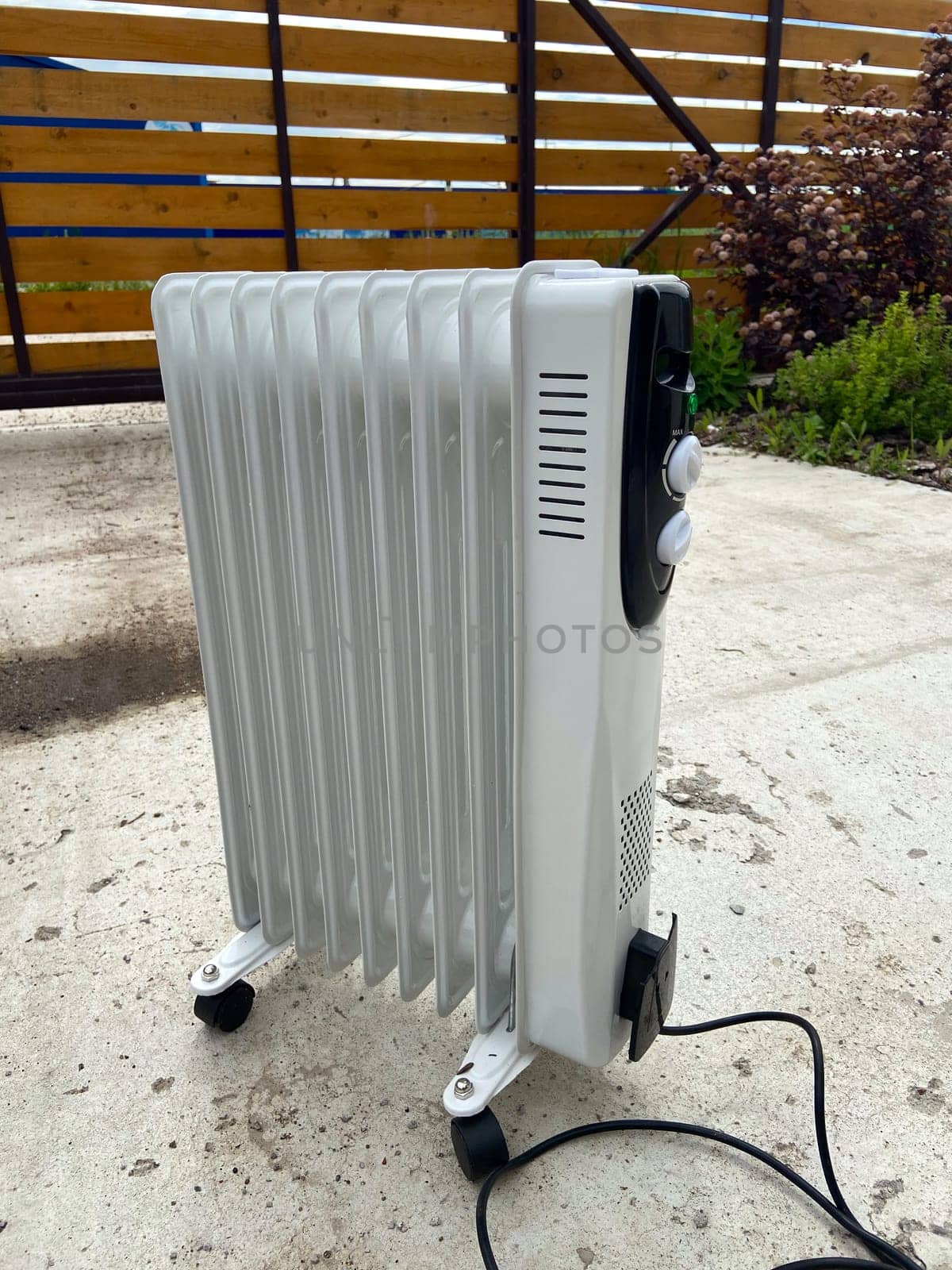 White oil-filled radiator stands outside on a concrete surface, prepared to provide warmth on a chilly day. Portable design makes it a practical heating solution for various environments.
