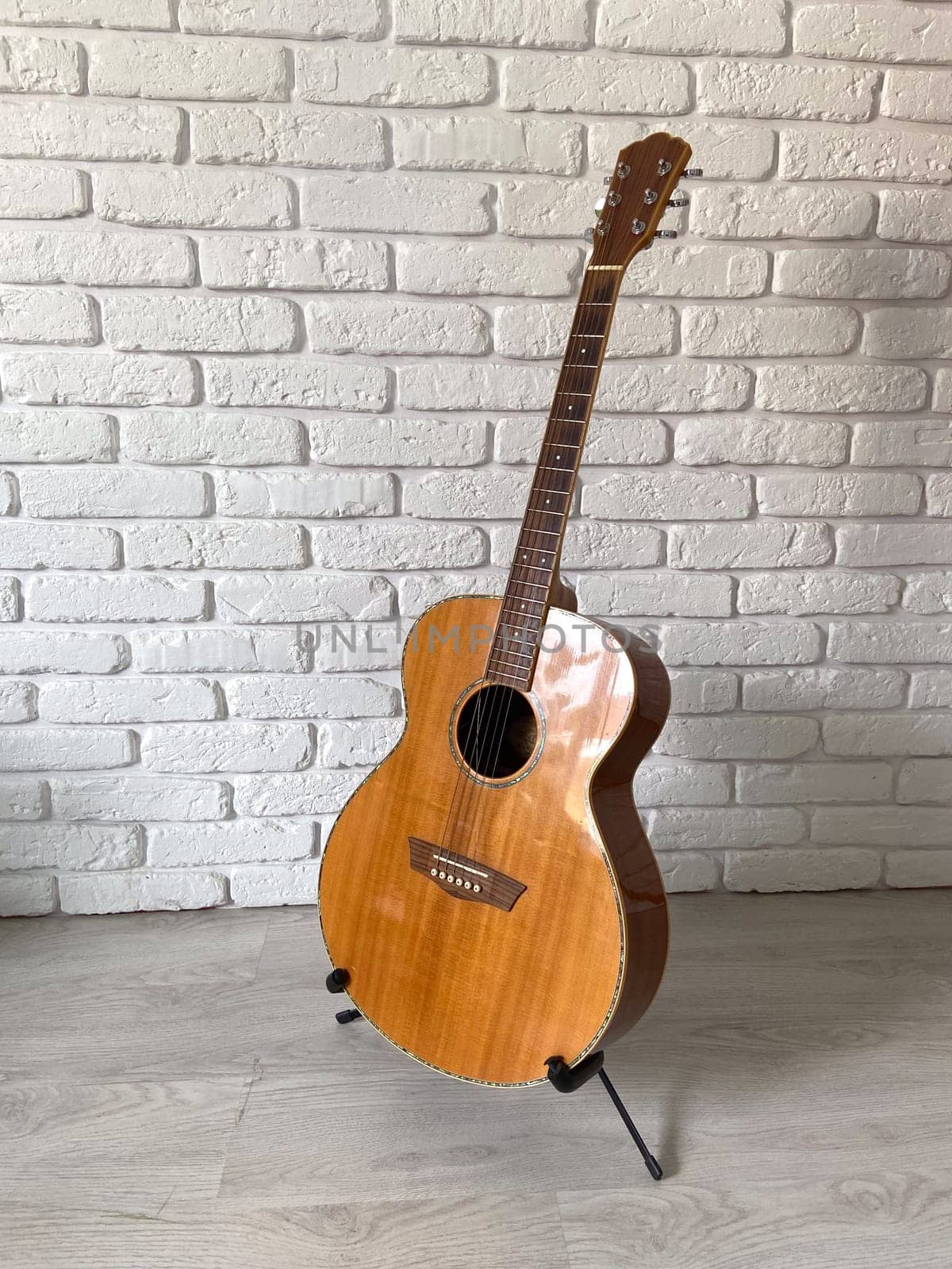 Wooden acoustic guitar stands elegantly against a textured white brick wall, creating a harmonious blend of music and art. Instrument craftsmanship.