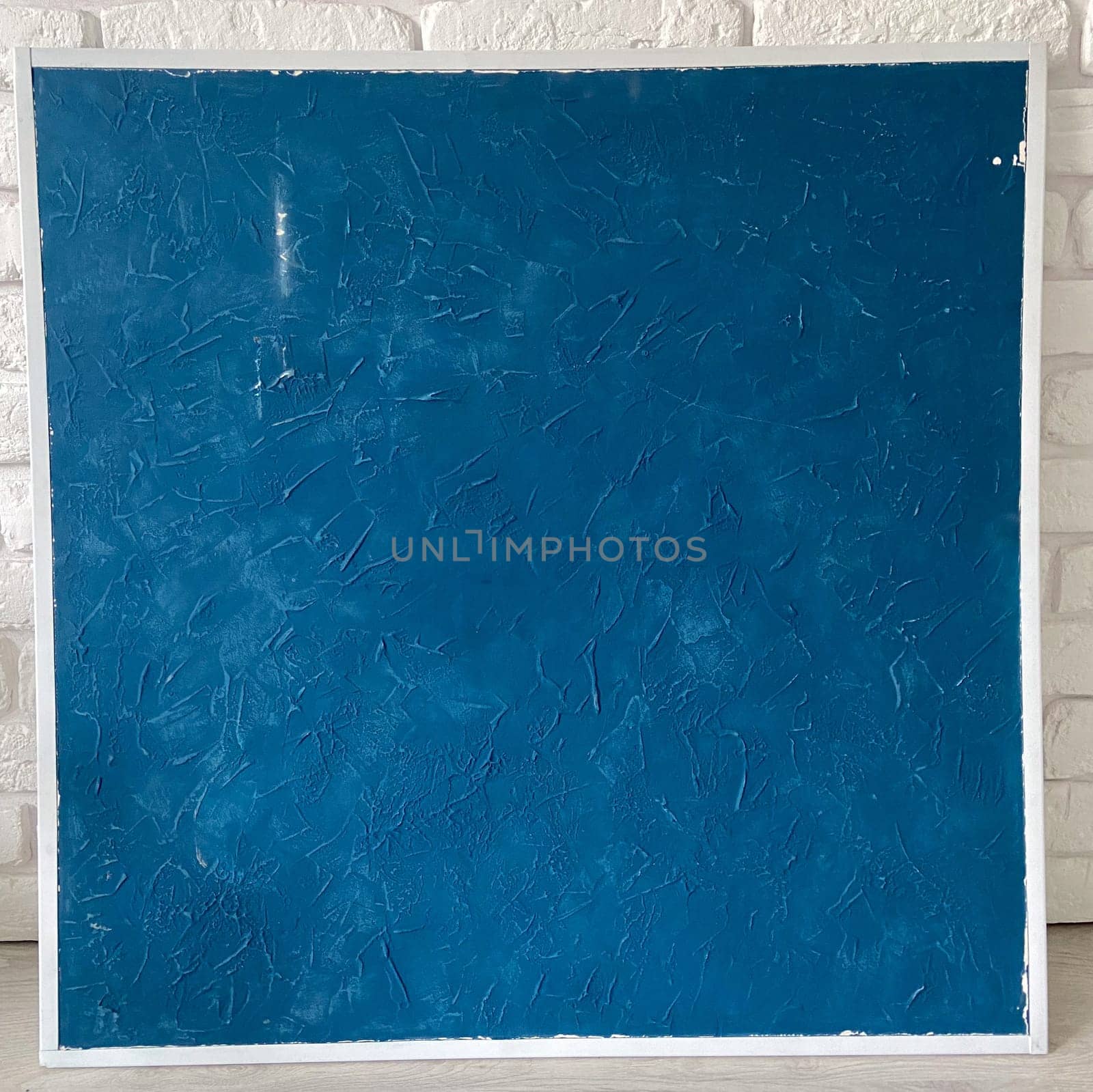 Textured deep blue panel is set against a white brick wall, emphasizing its rich color and intricate surface patterns. This composition reflects a perfect blend of modern art and minimalistic design, creating a striking visual impact.