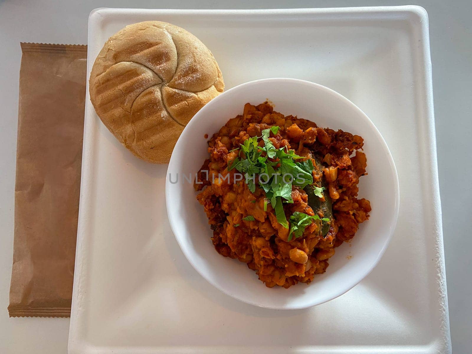 Delicious meal featuring a hearty bowl of stew garnished with herbs, served alongside fresh bread and a frothy coffee, is presented on a clean white tray. Inviting combination of flavors and textures perfect for a satisfying breakfast or lunch.