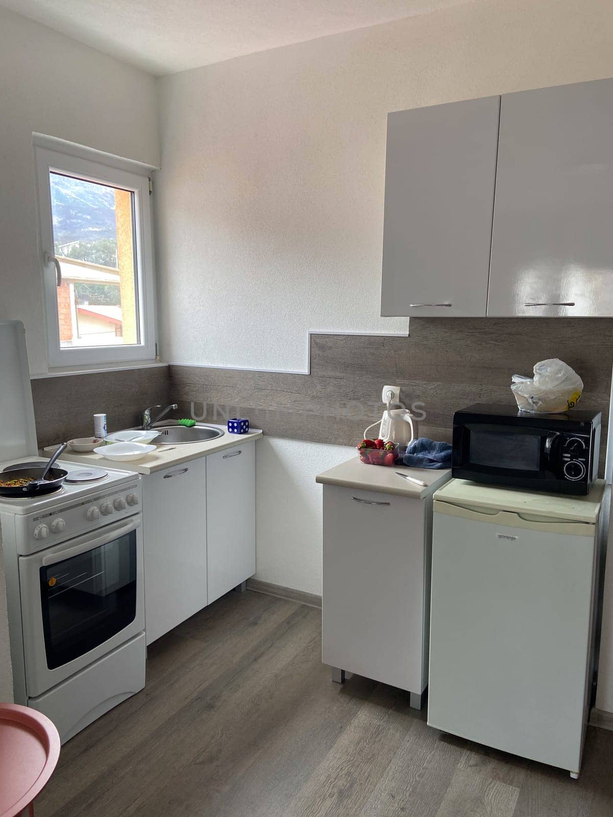 Compact modern kitchen with essential appliances and sleek cabinets is bathed in natural light from a nearby window. Minimalist space is perfect for efficient home cooking and preparing daily meals.