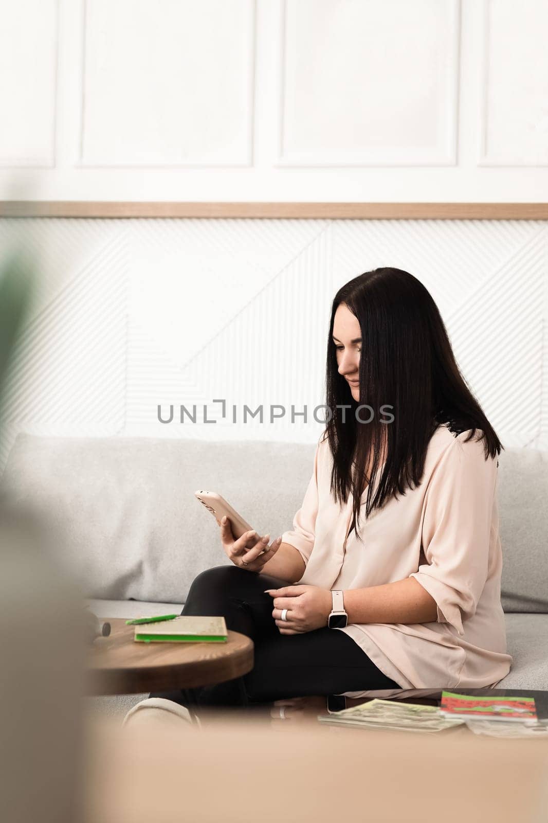 A brunette girl uses a mobile phone app, plays games, makes purchases online, orders delivery, relaxes on the couch.