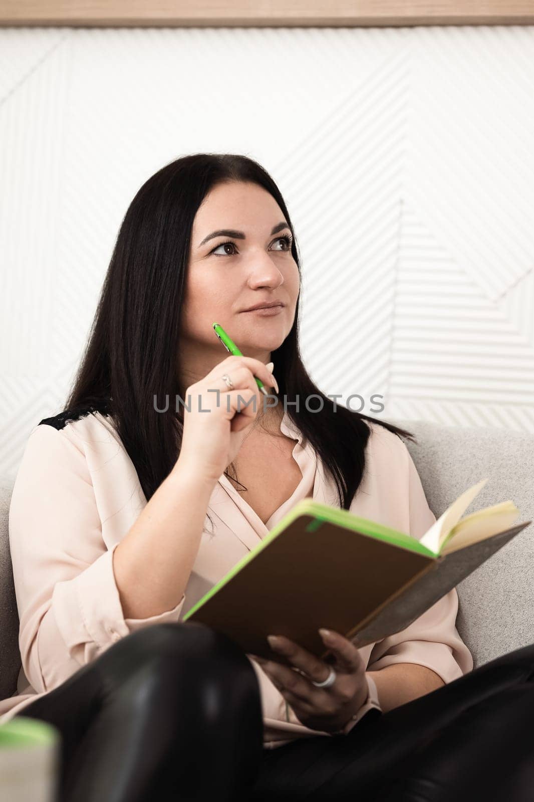 A woman is sitting comfortably on a cozy couch, thoughtfully writing and reflecting in her notebook