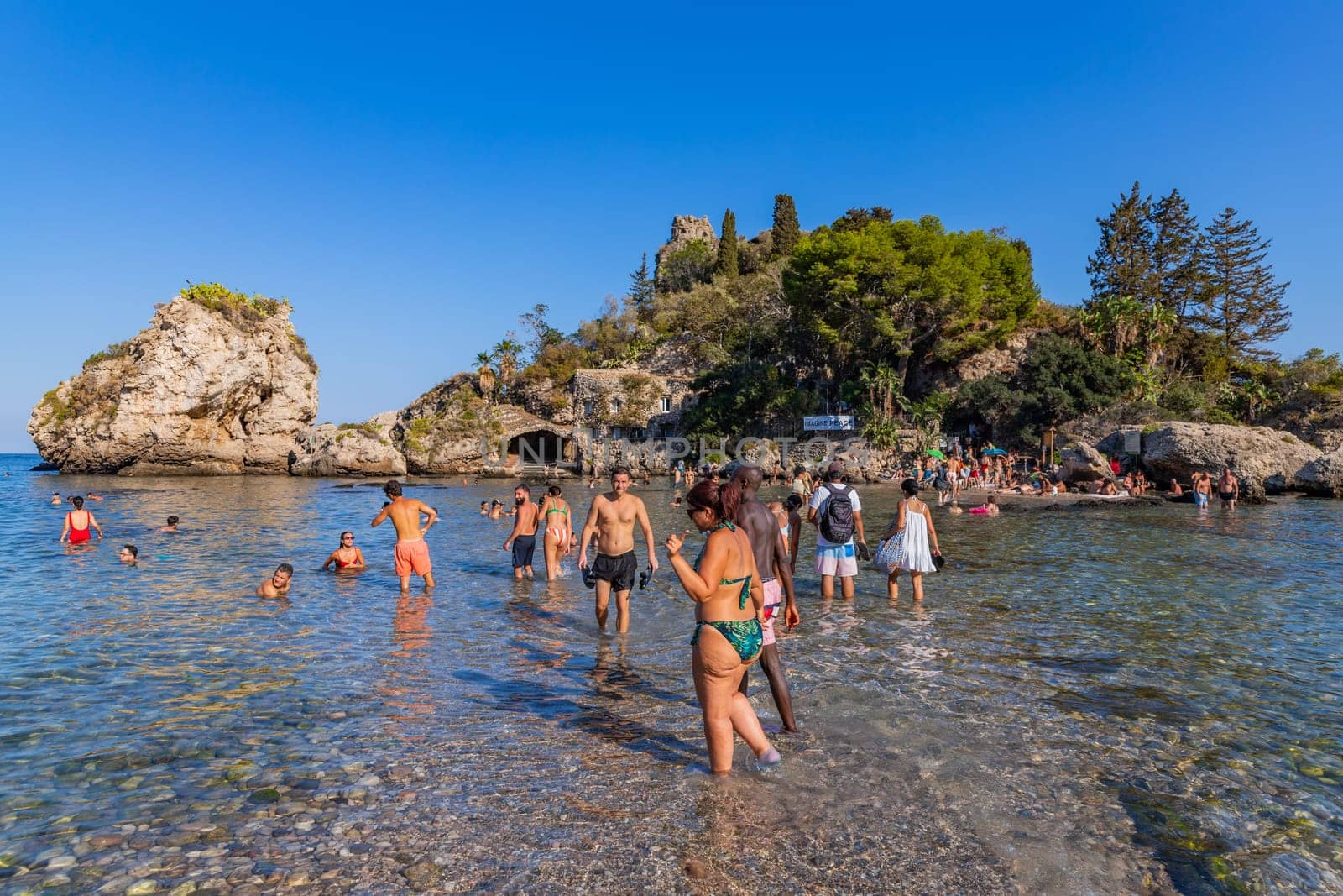 Taormina, Italy - August 11, 2024: People on the beach of Taormina with Isola Bella island on the background. Sicilia, Italy