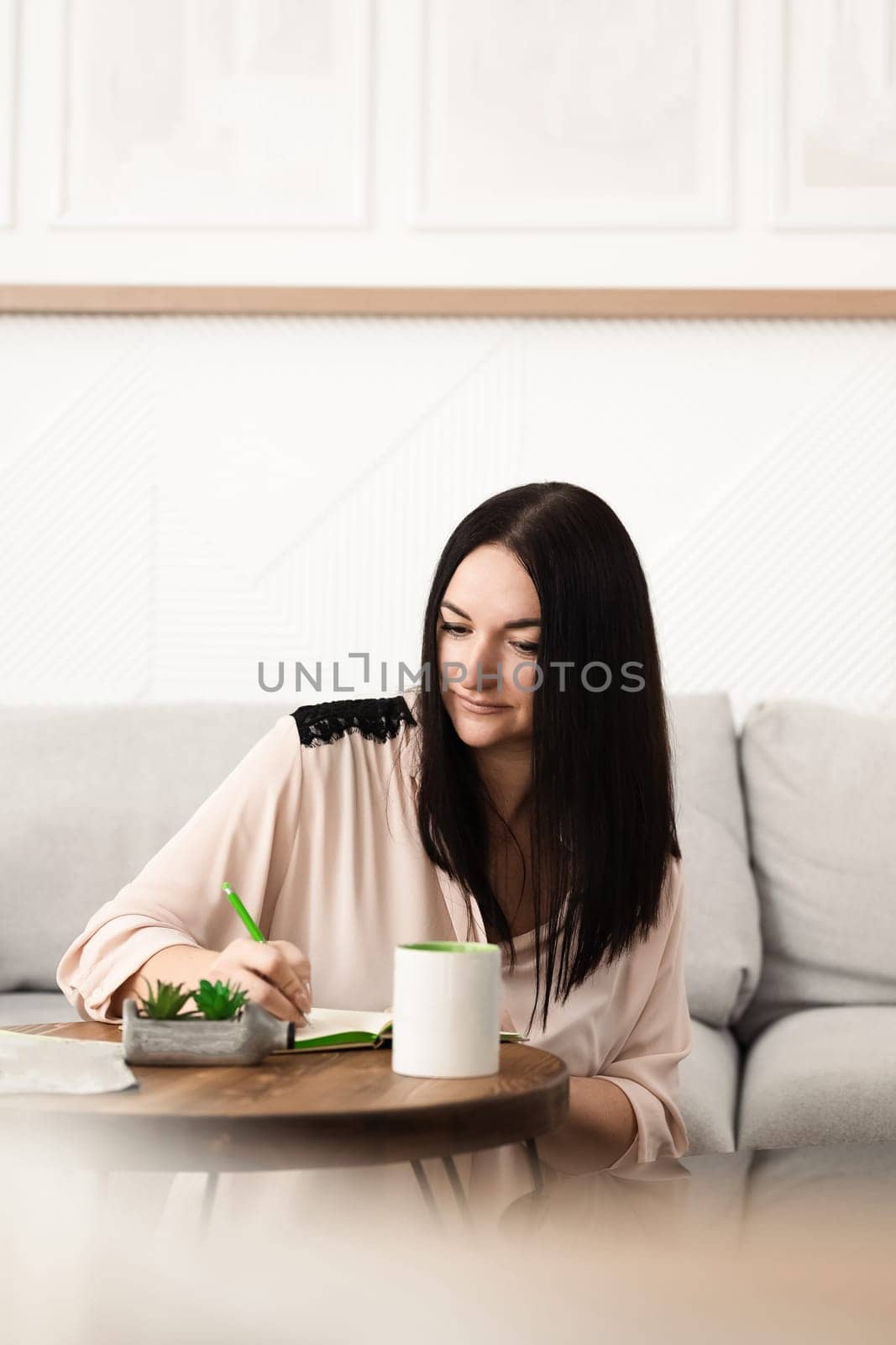 A brunette girl sitting at a desk in the office, making notes in a notebook on work with a mug of tea