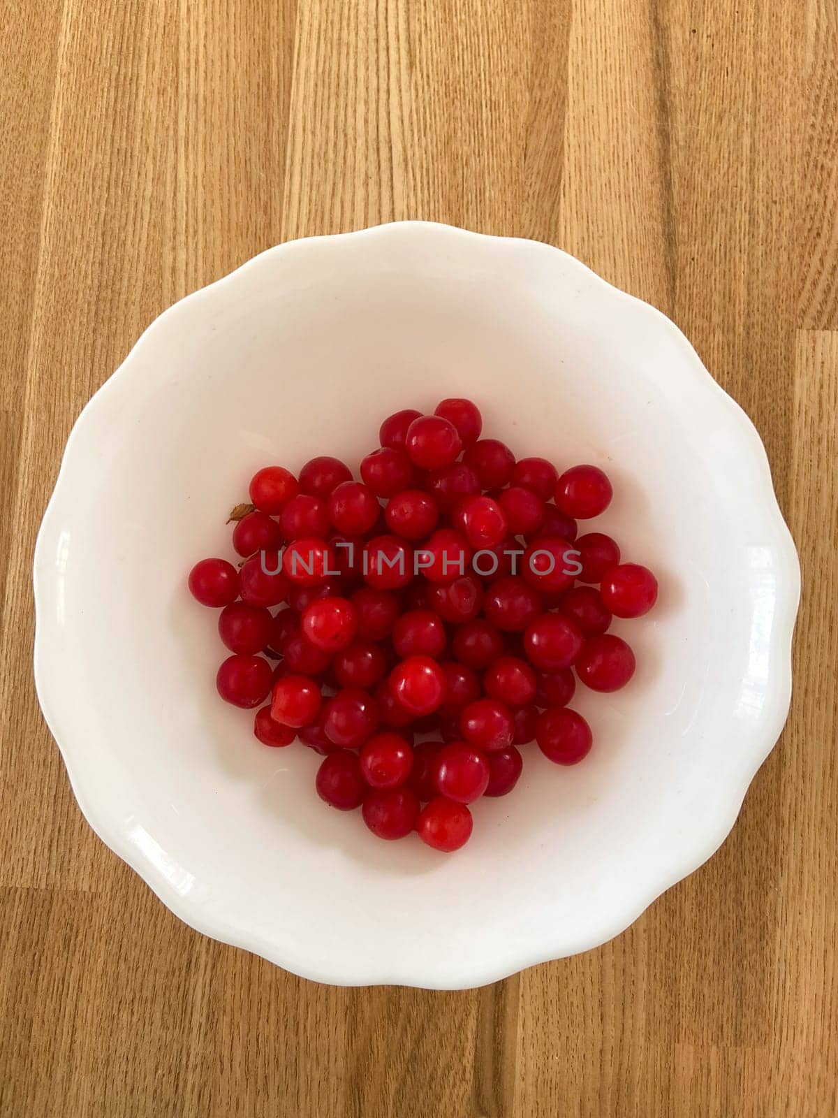 Collection of vibrant red berries sits elegantly in a white bowl, creating a striking contrast against a wooden background. Simple composition showcases the freshness and natural appeal of the fruit.
