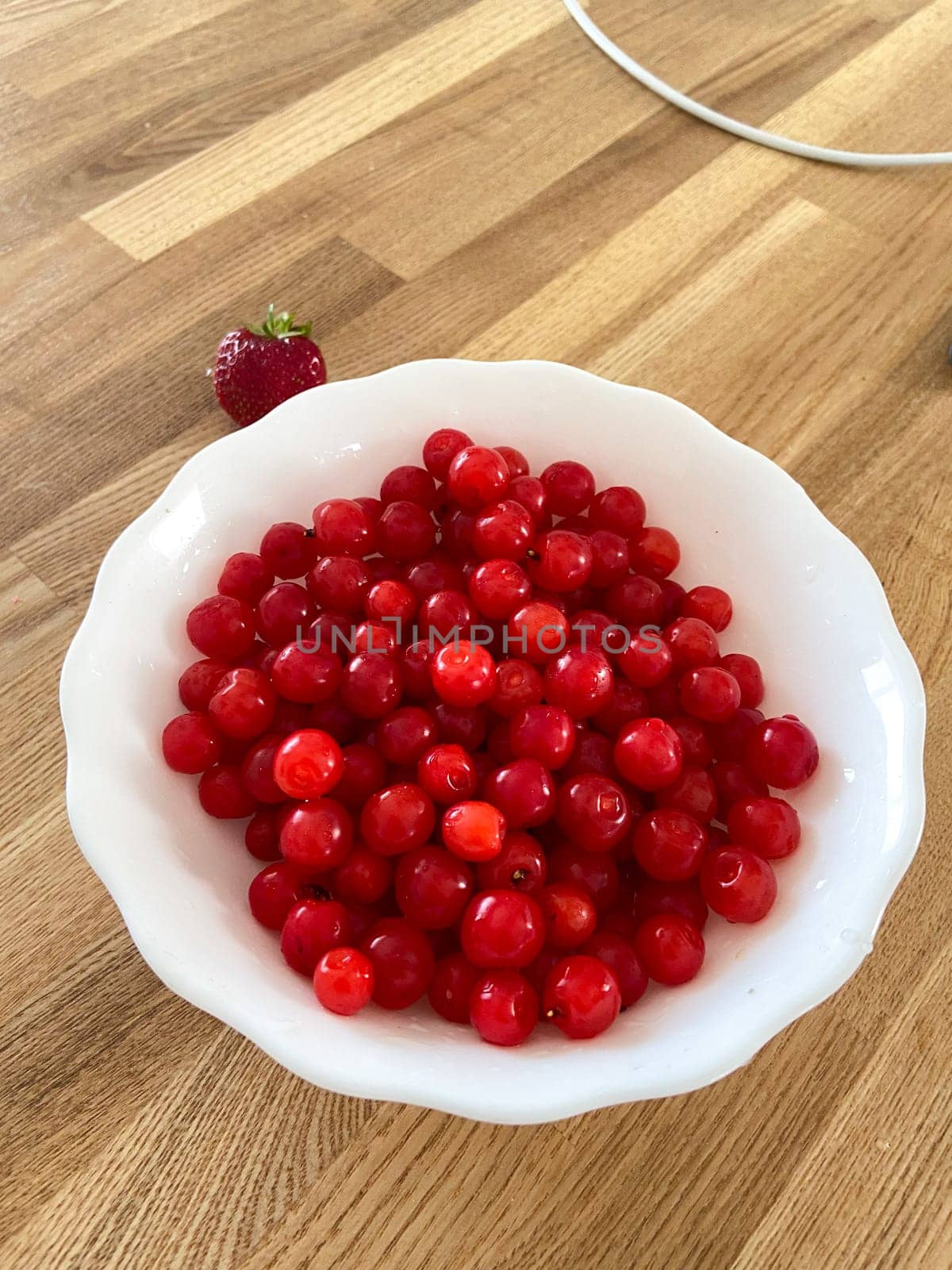 Collection of vibrant red berries sits elegantly in a white bowl, creating a striking contrast against a wooden background. Simple composition showcases the freshness and natural appeal of the fruit.