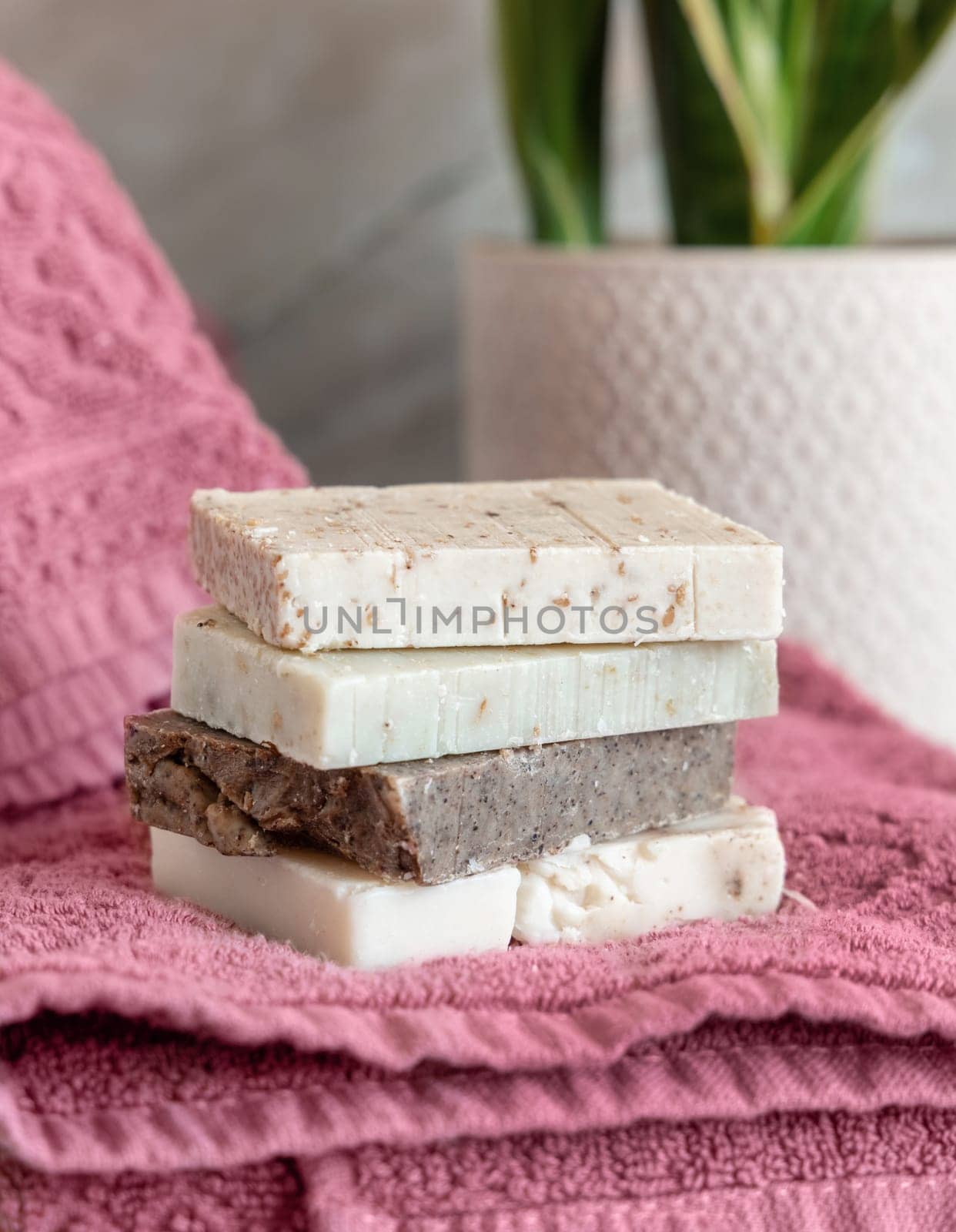Herbal Beige soap bars on pink folded towels near potted plant in bathroom, close up. Everyday Handmade hygiene product