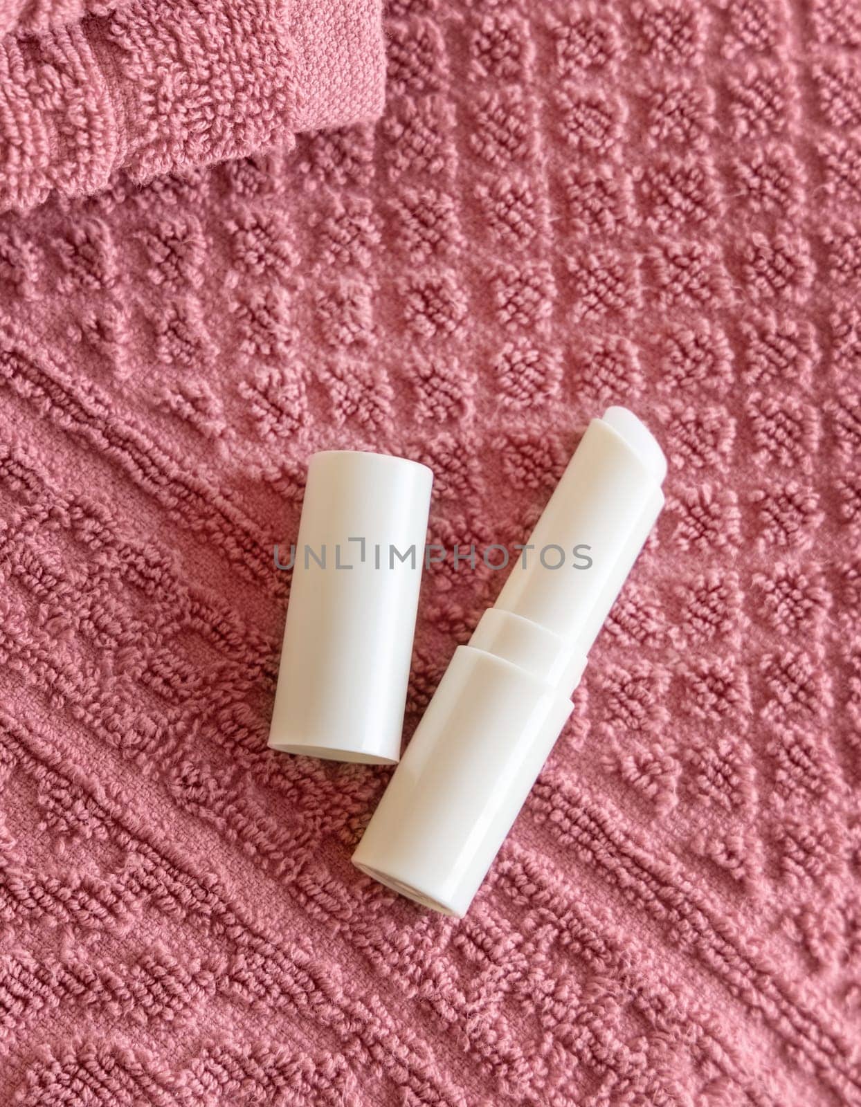 Opened white blank lip balm stick on dark grey folded towels, top view, cosmetic mockup. Lifestile scene with lipcare product, everyday personal care