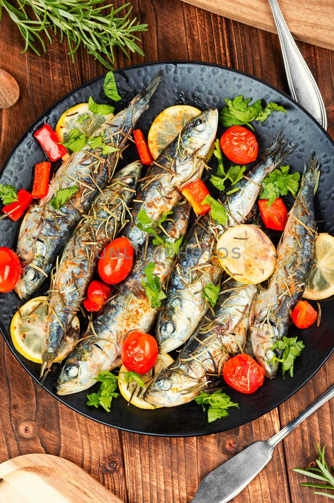 Baked sardine fish with lemon, cherry tomatoes and rosemary on rustic wooden table. Healthy and tasty dinner. Rustic style.