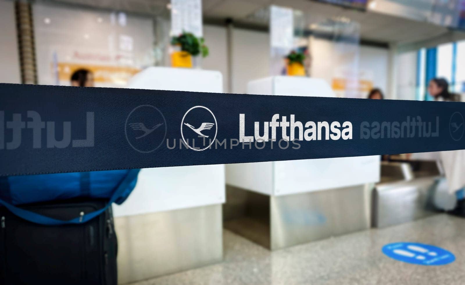 Lufthansa branded barrier in airport check-in area. Focus on branded tape with blurred background of counters and passengers. Travel and airline industry concept