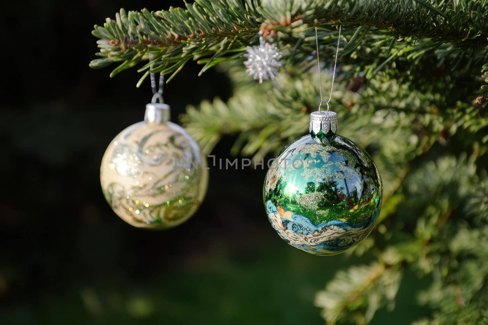 Two colorful Christmas ornaments hang from a tree branch showcasing intricate designs and vibrant colors in a serene outdoor setting.