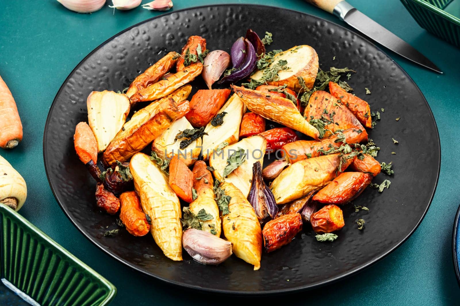Roasted root vegetables, baked parsnip root, red onions, carrots, and garlic for a vegan dish.
