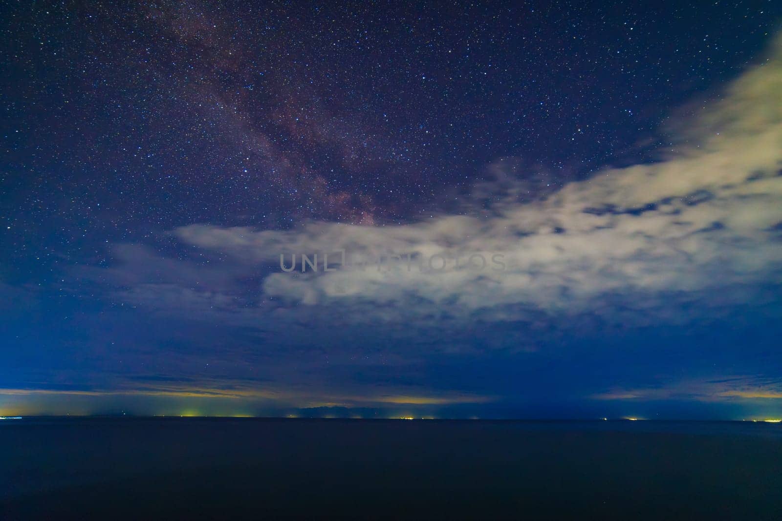 starry night sky with few clouds over large mountain lake at night