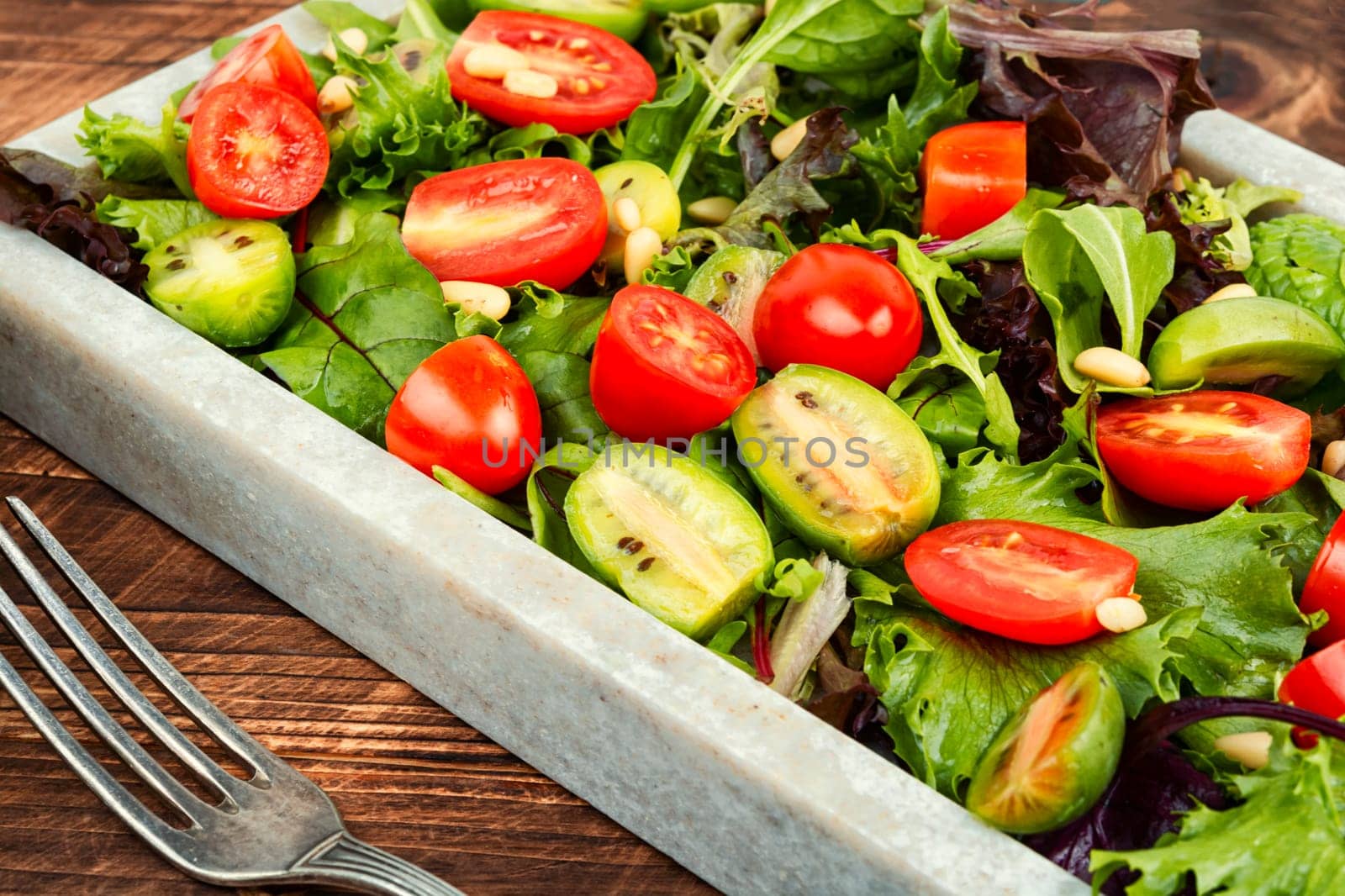 Homemade vegetarian salad with greens, colorful cherry tomatoes on a stylish stone tray. Vegan meal. Flat lay