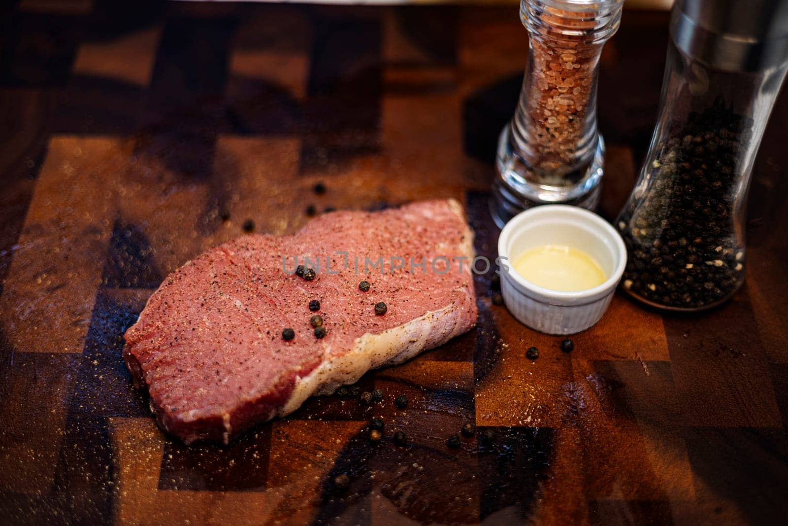 Raw meat steak with seasonings on wooden cutting board.