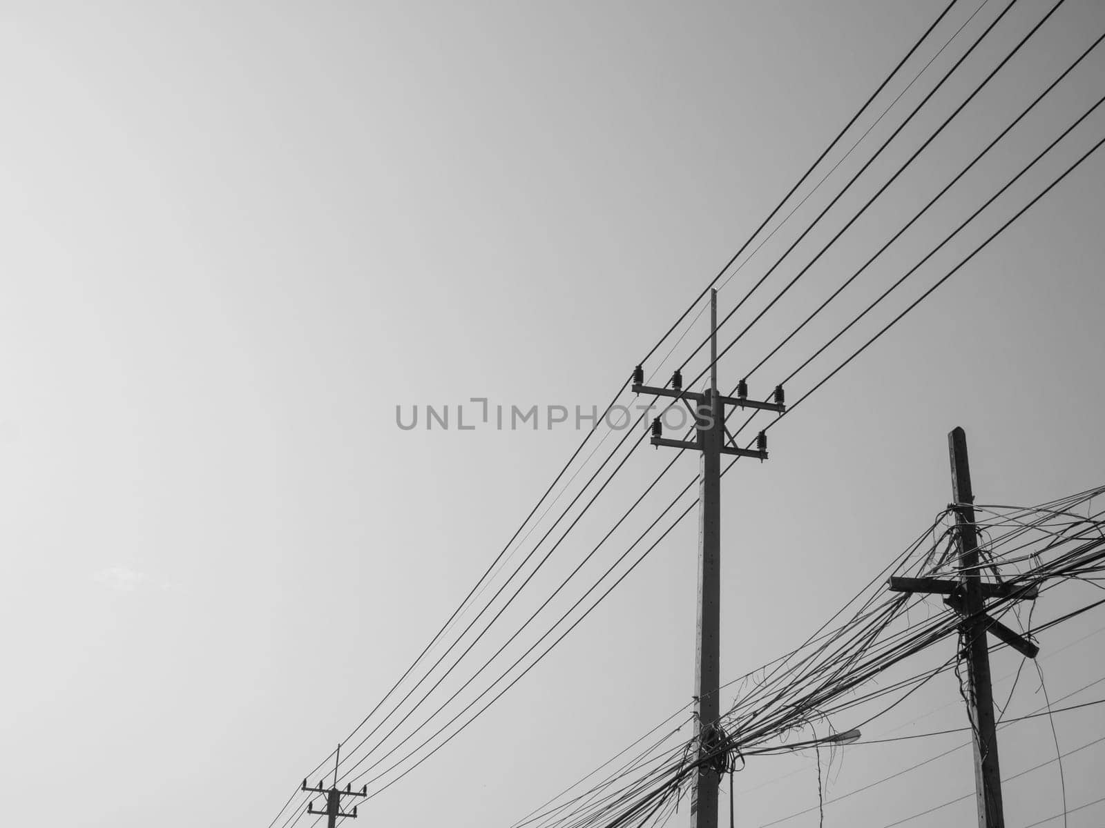 Black and white photo of Reinforced concrete pillar with high-voltage wires against a clear sky. Transmission of electricity by wires over long distances. Electricity power lines against a clear sky.