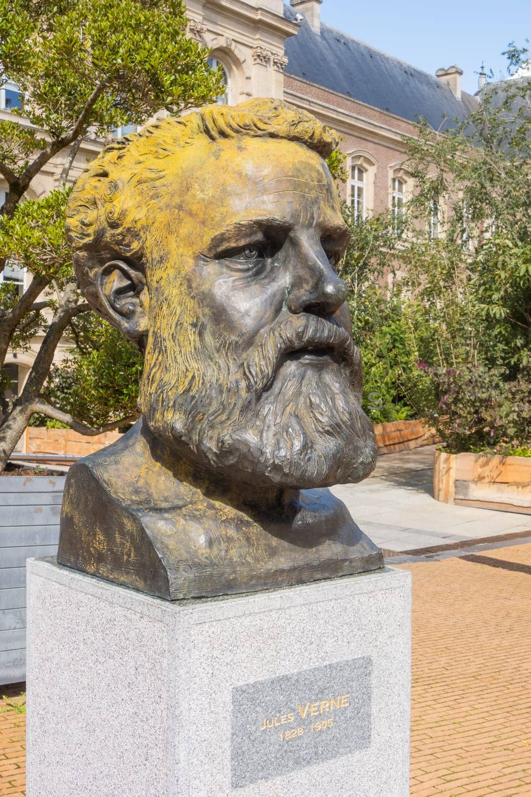 Amiens, France – September 12, 2024: City Hall and bronze buste of Jules Verne, famous French writer and adventurer, by artist and sculptor Philippe Arnault, vertical