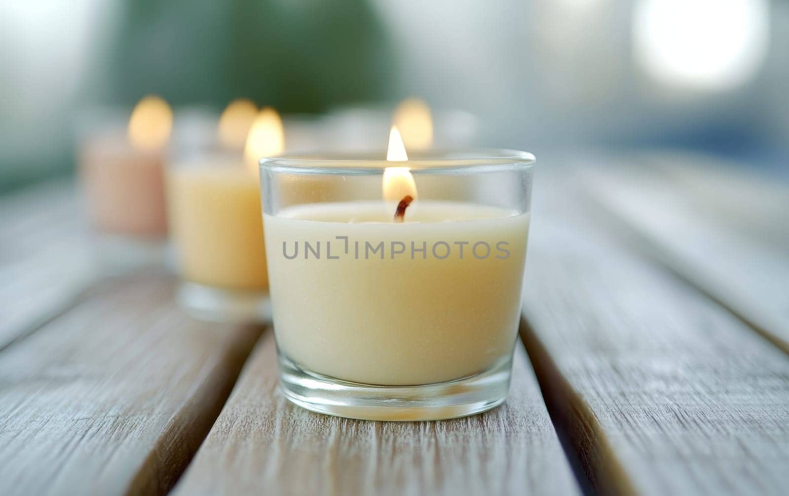 Lit scented candles in glass jars on a wooden surface, creating a tranquil atmosphere. Soft focus background suggests relaxation and spa ambiance.