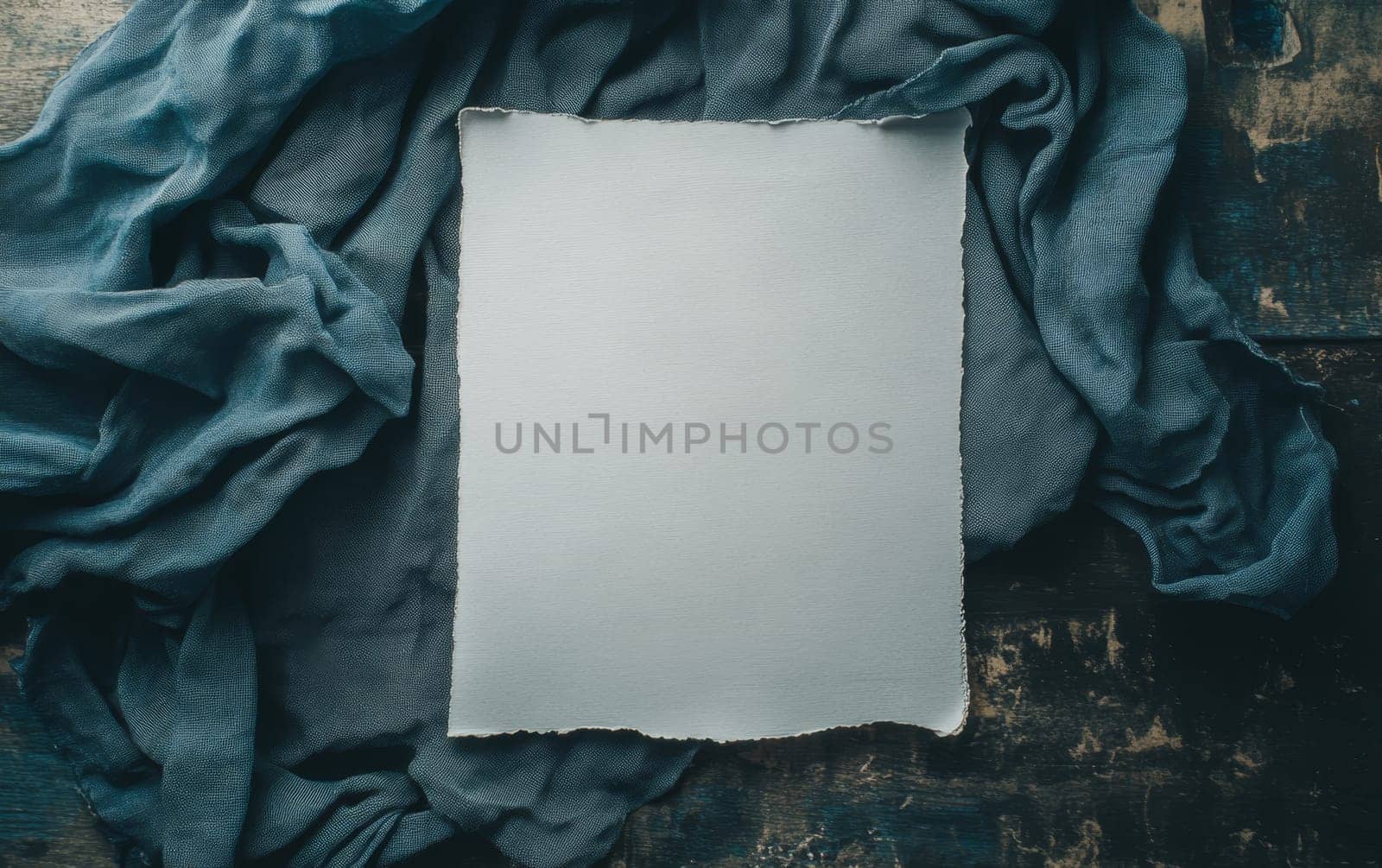 White torn paper with copy space surrounded by crumpled teal fabric on rustic wooden surface. Vintage style flat lay with room for text.
