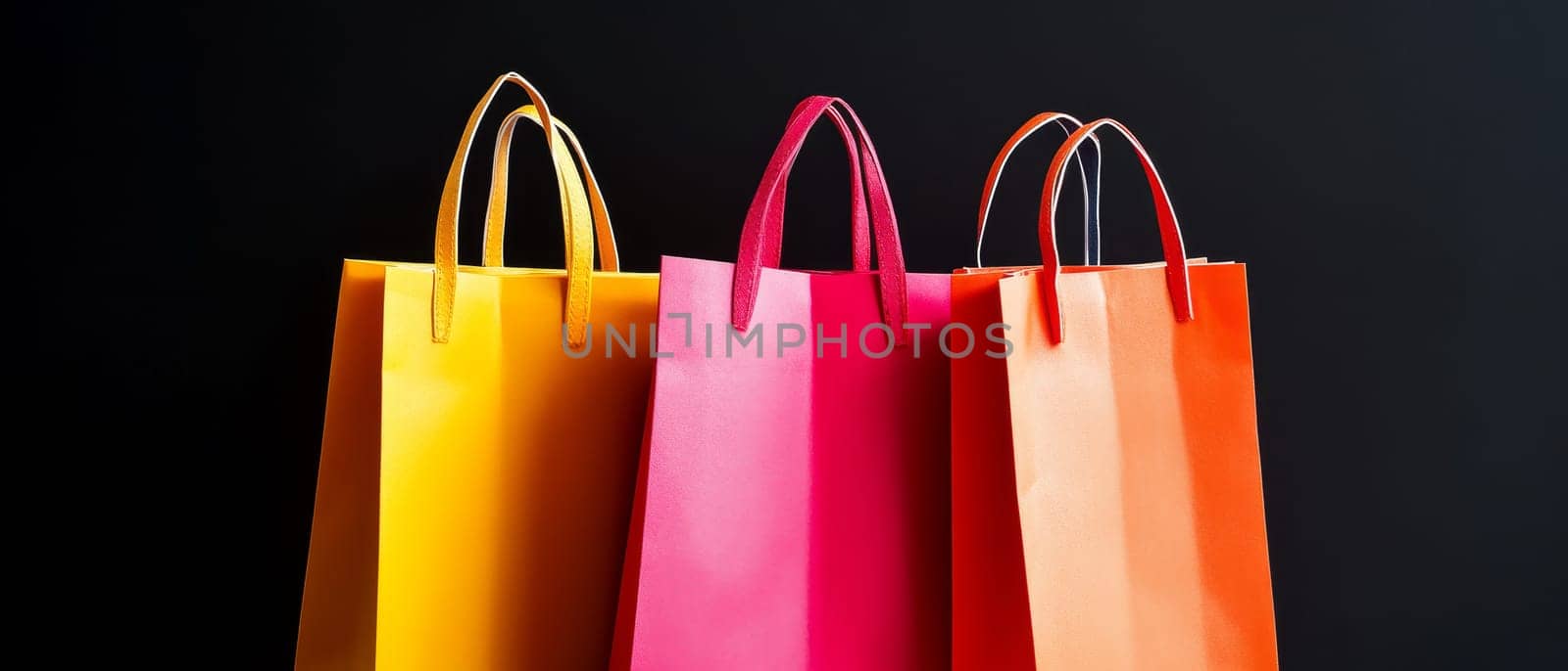 Vibrant shopping bags in yellow, pink, and orange against a black backdrop, representing retail and fashion. Black Friday sale concept with place for text.