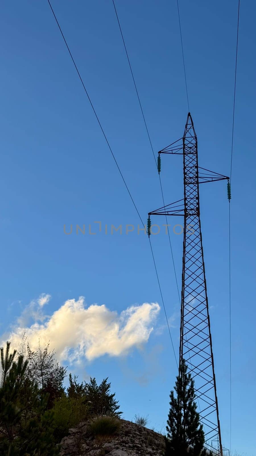 A tall power line tower stretches toward a clear blue sky with light clouds. nature and industrial technology.
