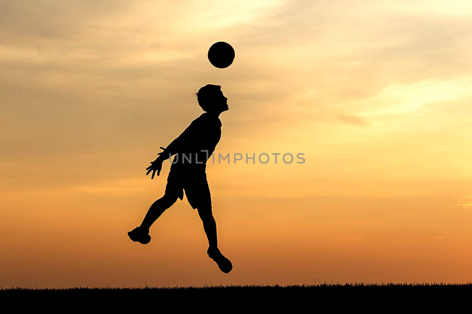 A young athlete heads a soccer ball at sunset in this concept photo.