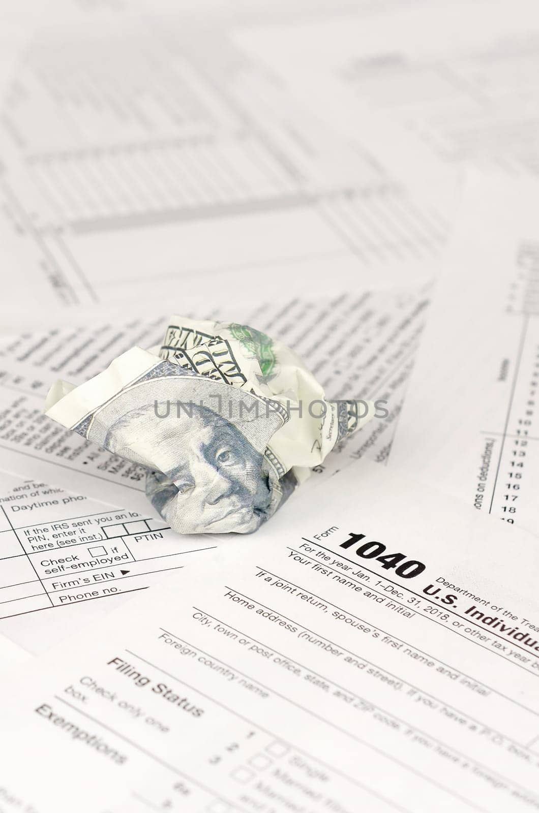 1040 Individual income tax return form and crumpled hundred dollar bill. Loss of money to pay taxes concept