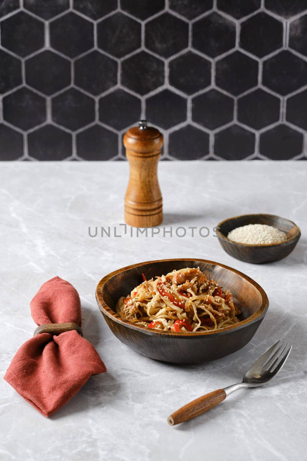 An appetizing plate of pasta with pulled beef in a rustic brown bowl, garnished with vegetables and sesame seeds.