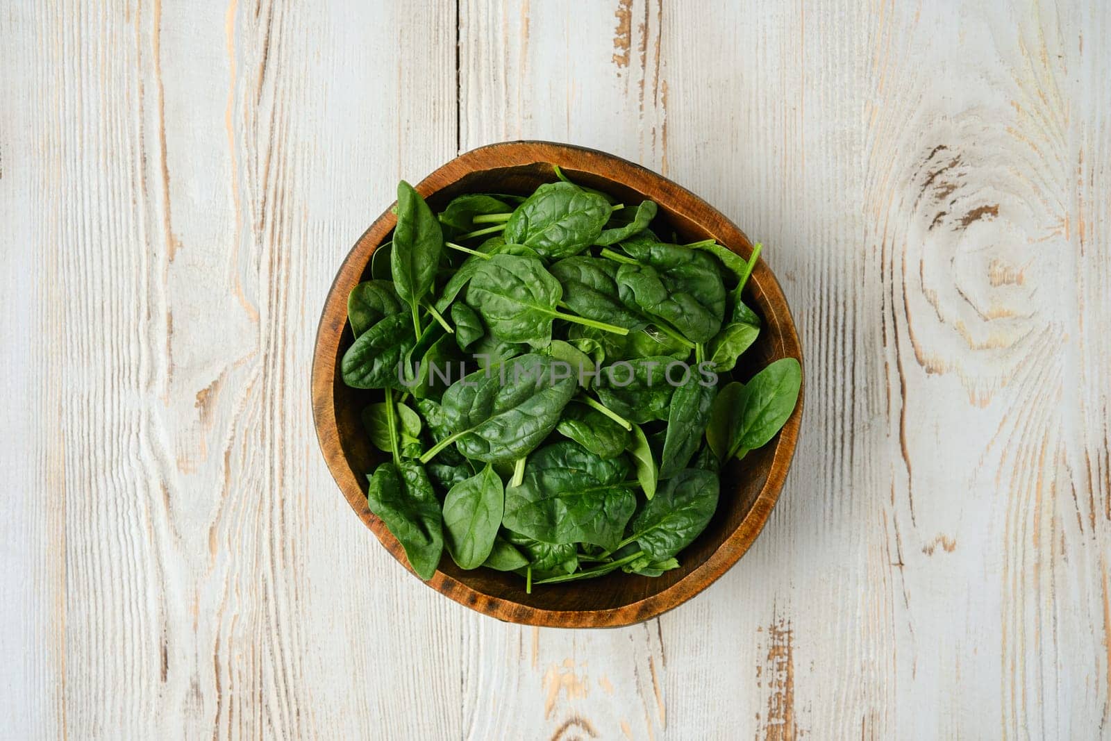 A wooden bowl filled with vibrant green spinach leaves rests on a rustic wooden table, showcasing the freshness of the greens. Perfect for salads, smoothies, or healthy dishes.