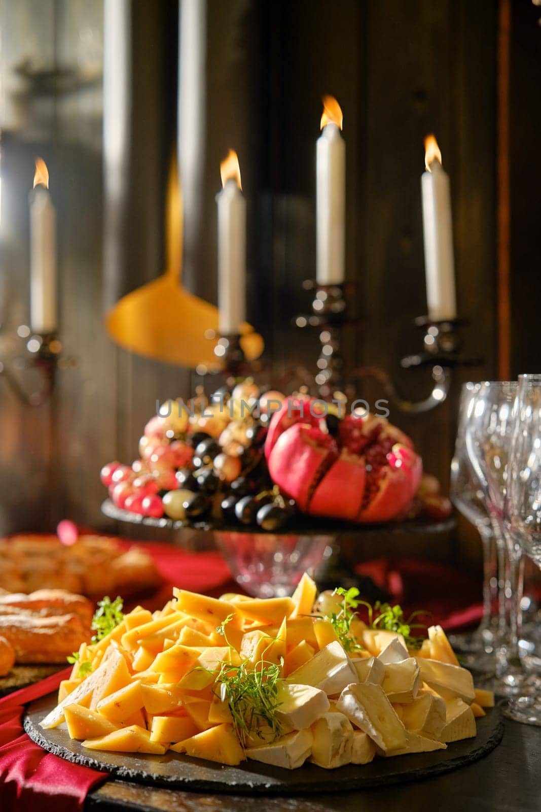A beautifully arranged cheese platter features an assortment of cheeses alongside a colorful fruit display. Elegant candles illuminate the table, creating a warm atmosphere perfect for a gathering.