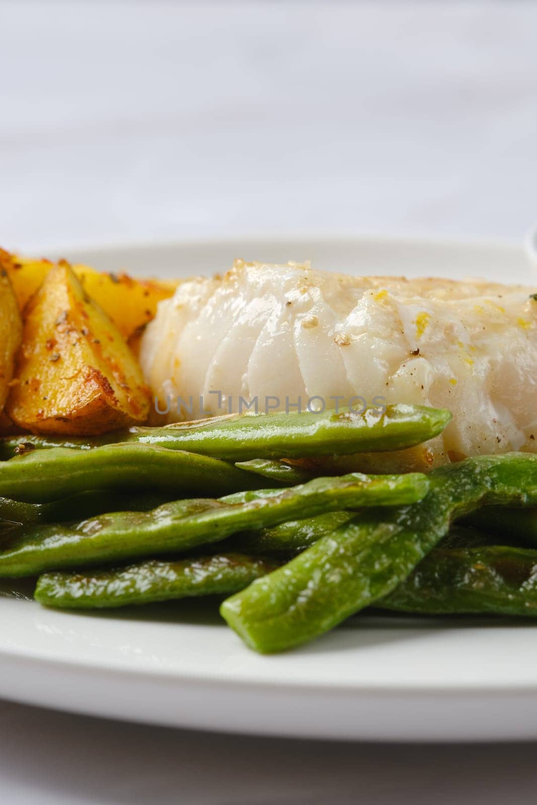 A plate showcases tender white fish alongside perfectly roasted golden potatoes and vibrant green beans. The dish highlights fresh ingredients, ideal for a nutritious and satisfying meal.