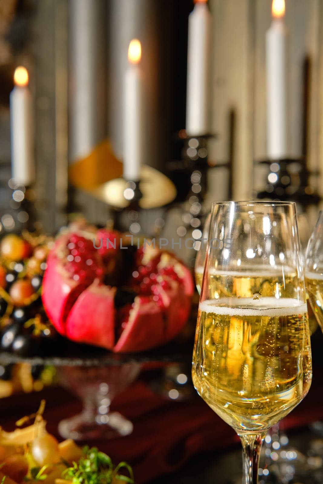 A beautifully arranged table features sparkling champagne flutes and a vibrant array of seasonal fruits, including pomegranate, all illuminated by soft candlelight for a festive vibe.