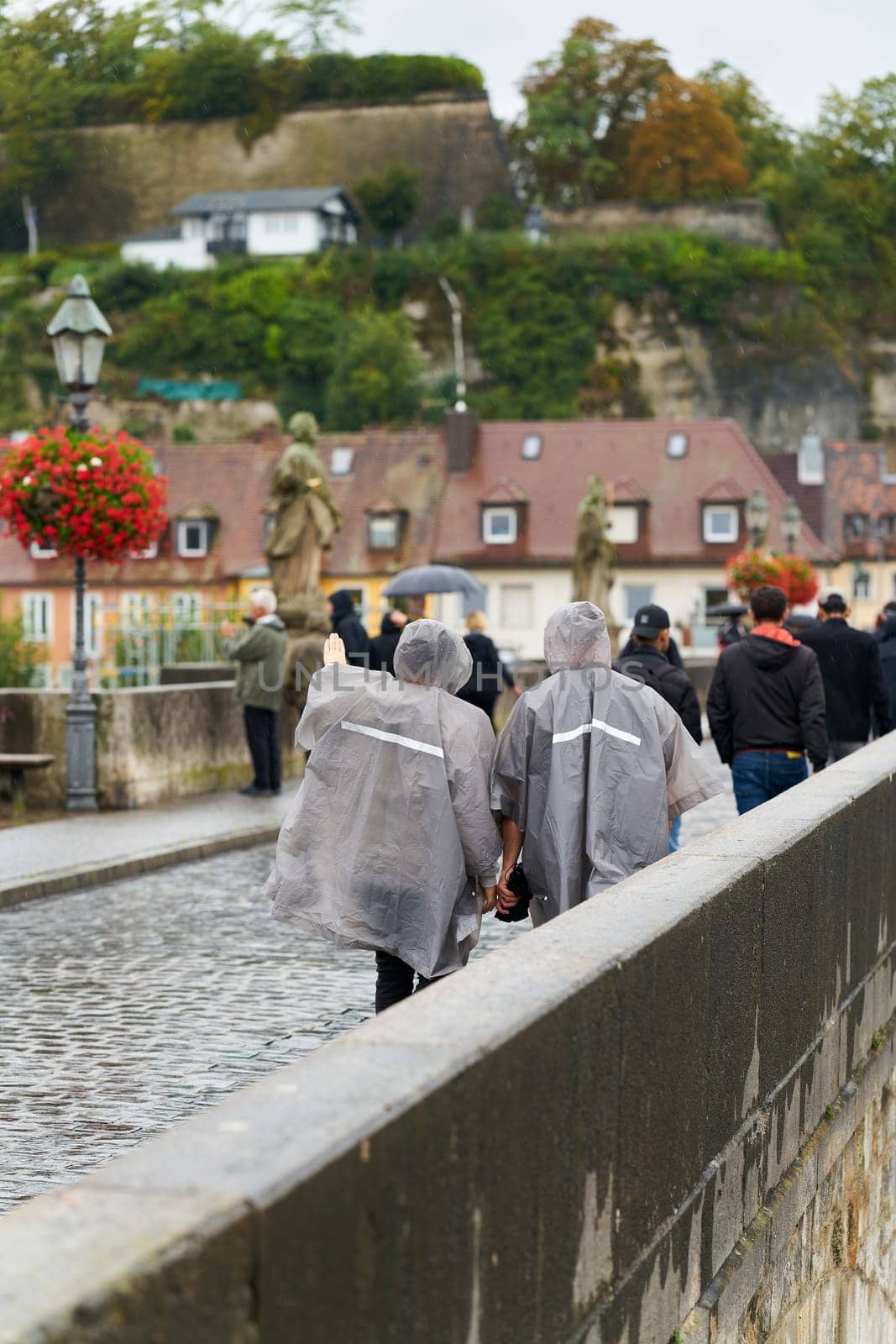 Tourists with rain wear walking across the old Main bridge, alte Mainbrucke in Würzburg in Germany in the rain