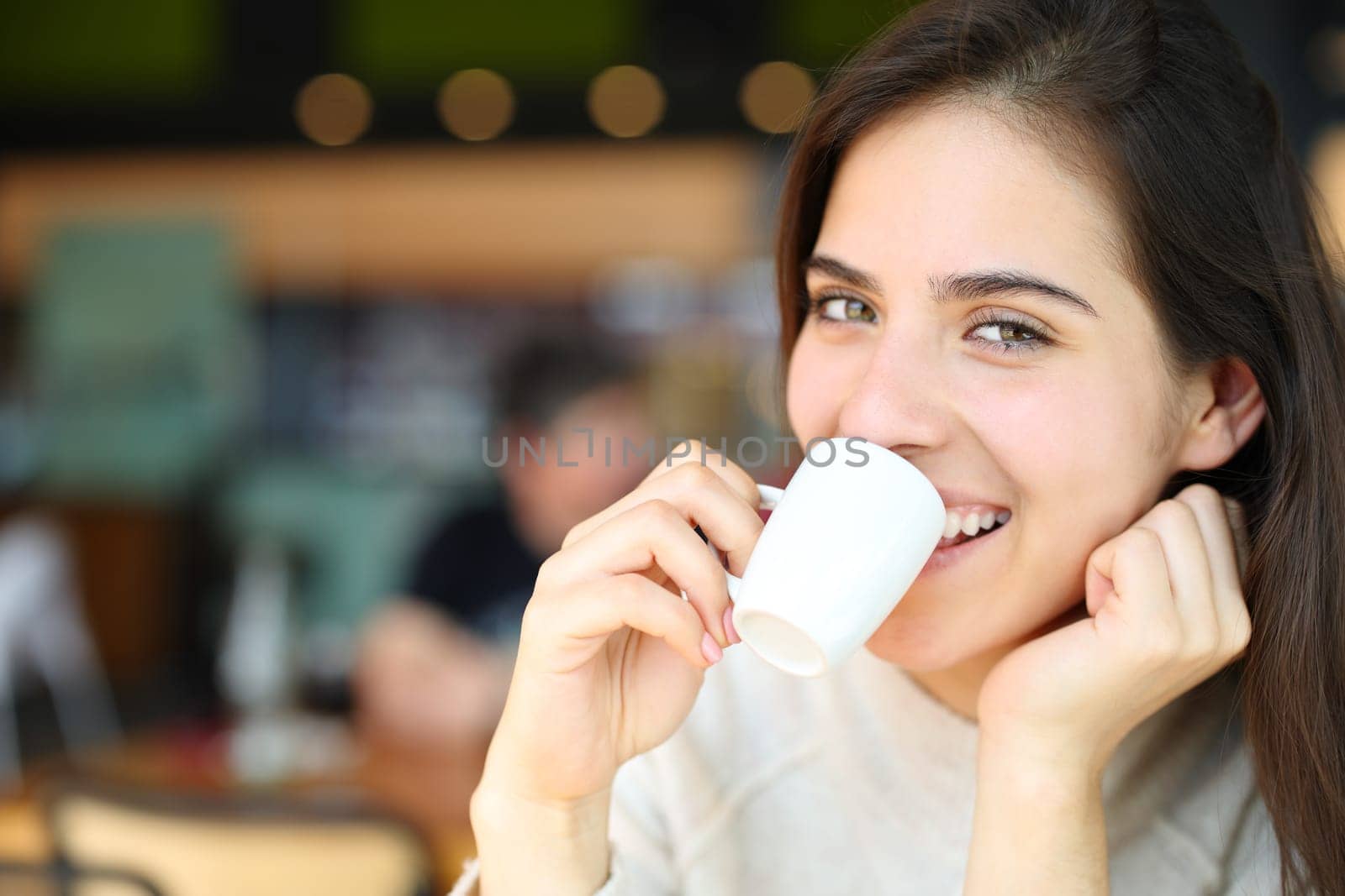 Happy woman drinking coffee in a bar looks at you smiling