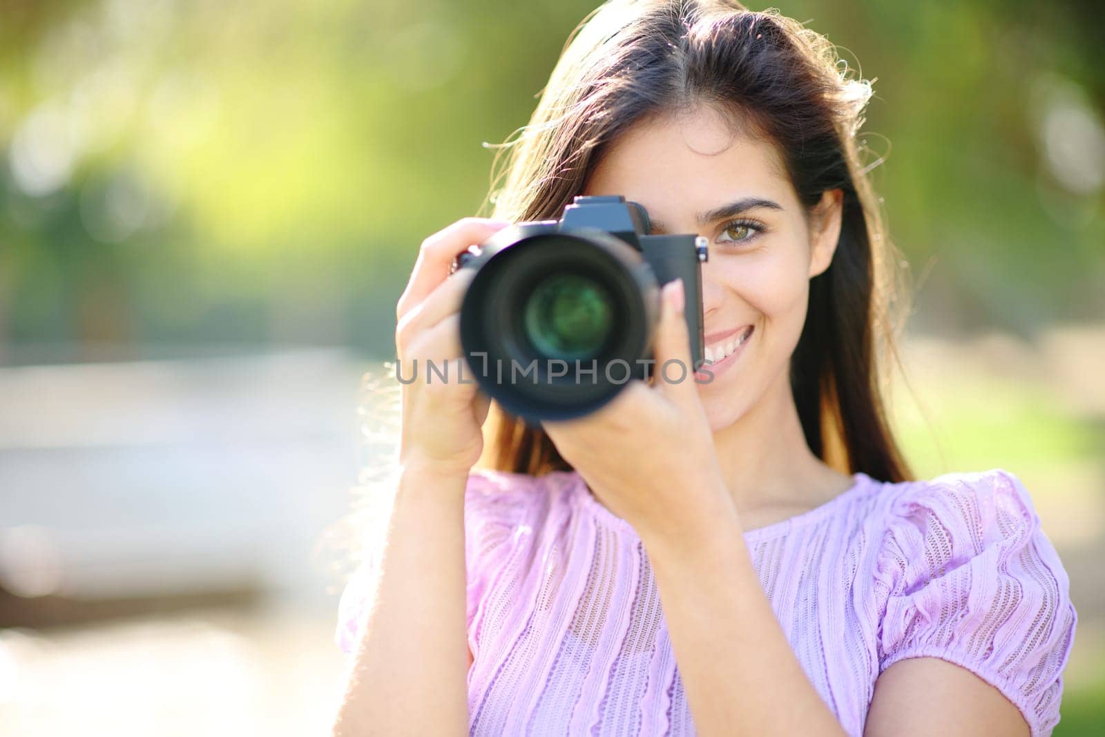 Happy photographer taking picture of you with mirrorless camera in a park