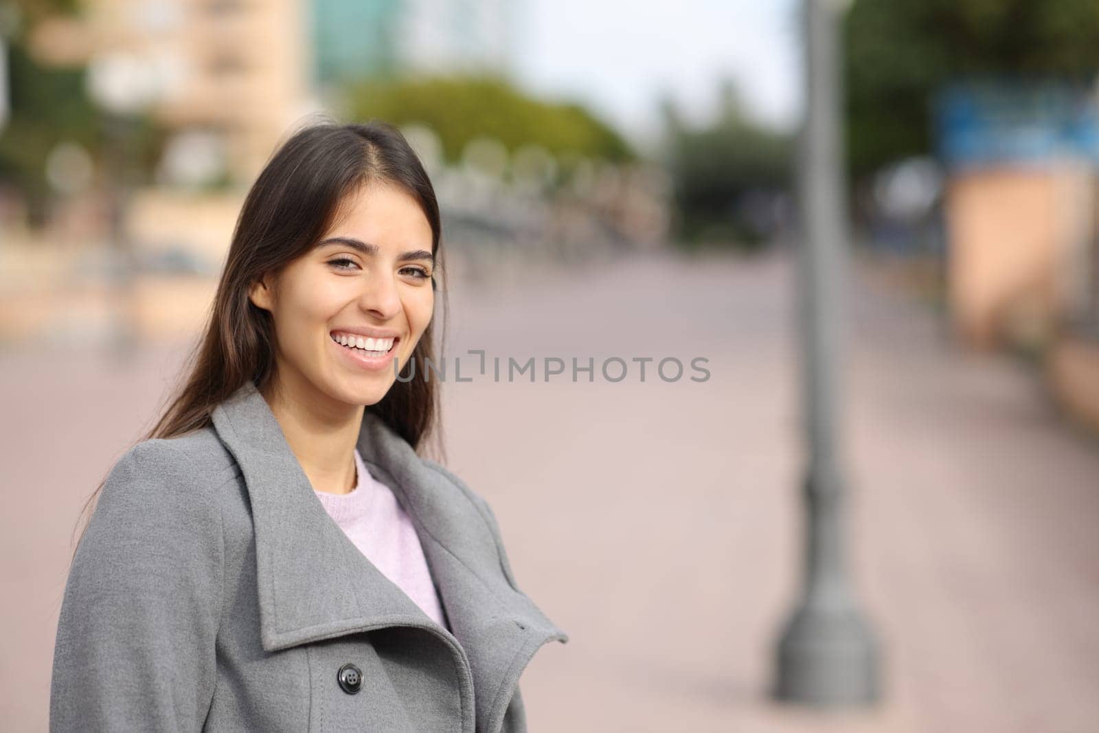 Happy woman in winter laughing standing in the street looks at you
