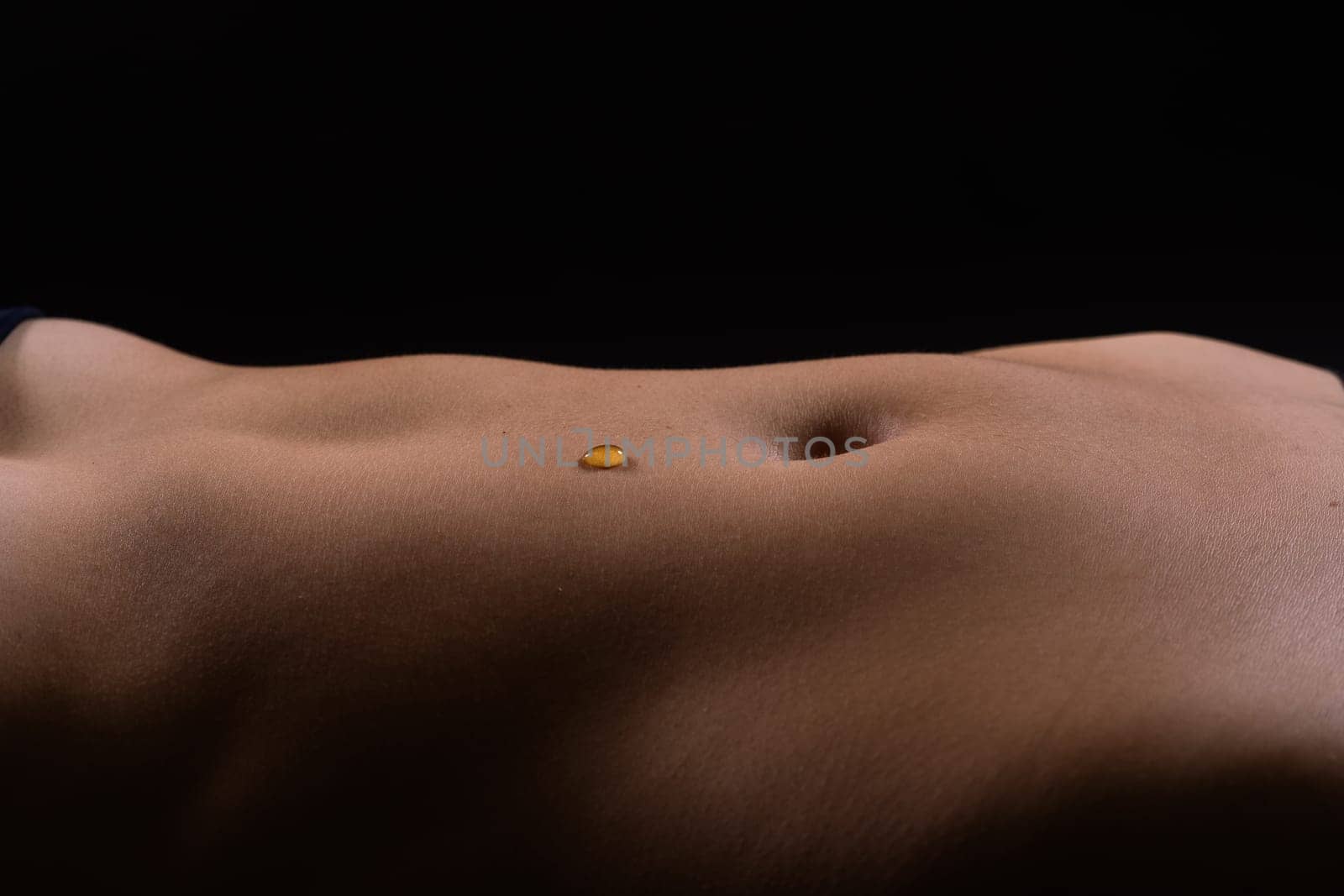 Beautiful seductive young female makes honey on a black background. Drops of honey on her belly.
