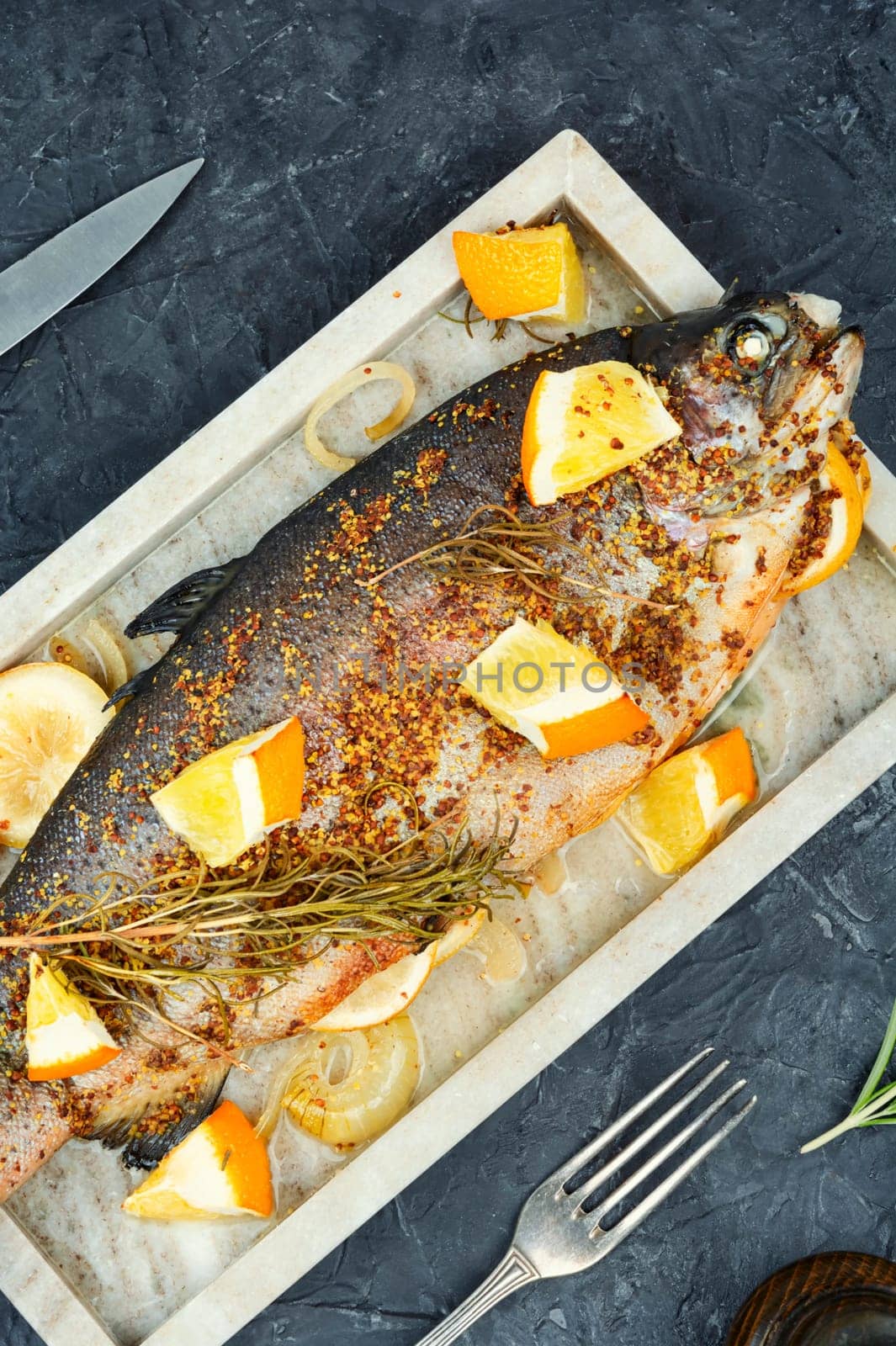 Trout fried with orange and rosemary on wooden background.