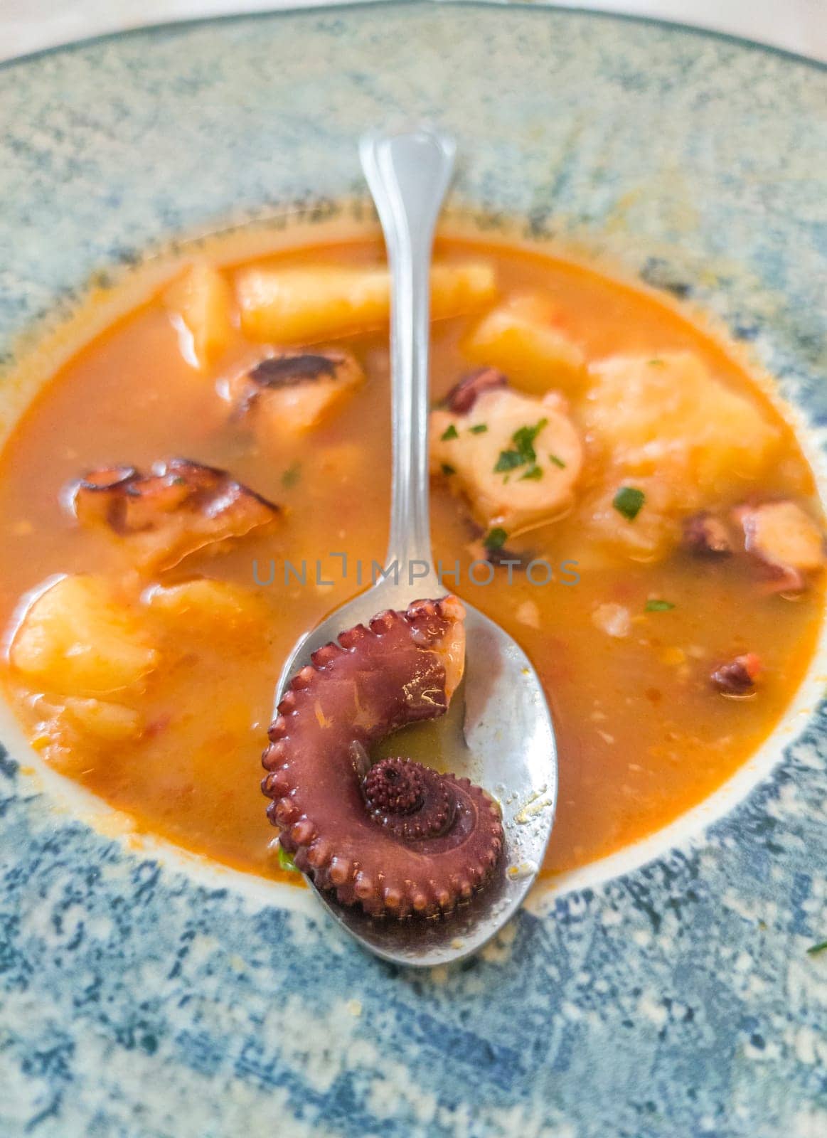 Potato stew with seafood displayed over table. Octopus tentacle on spoon in close-up