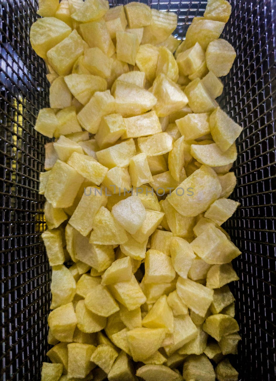 Basket of dices potatoes in the deep fryer of a restaurant kitchen. Overhead view