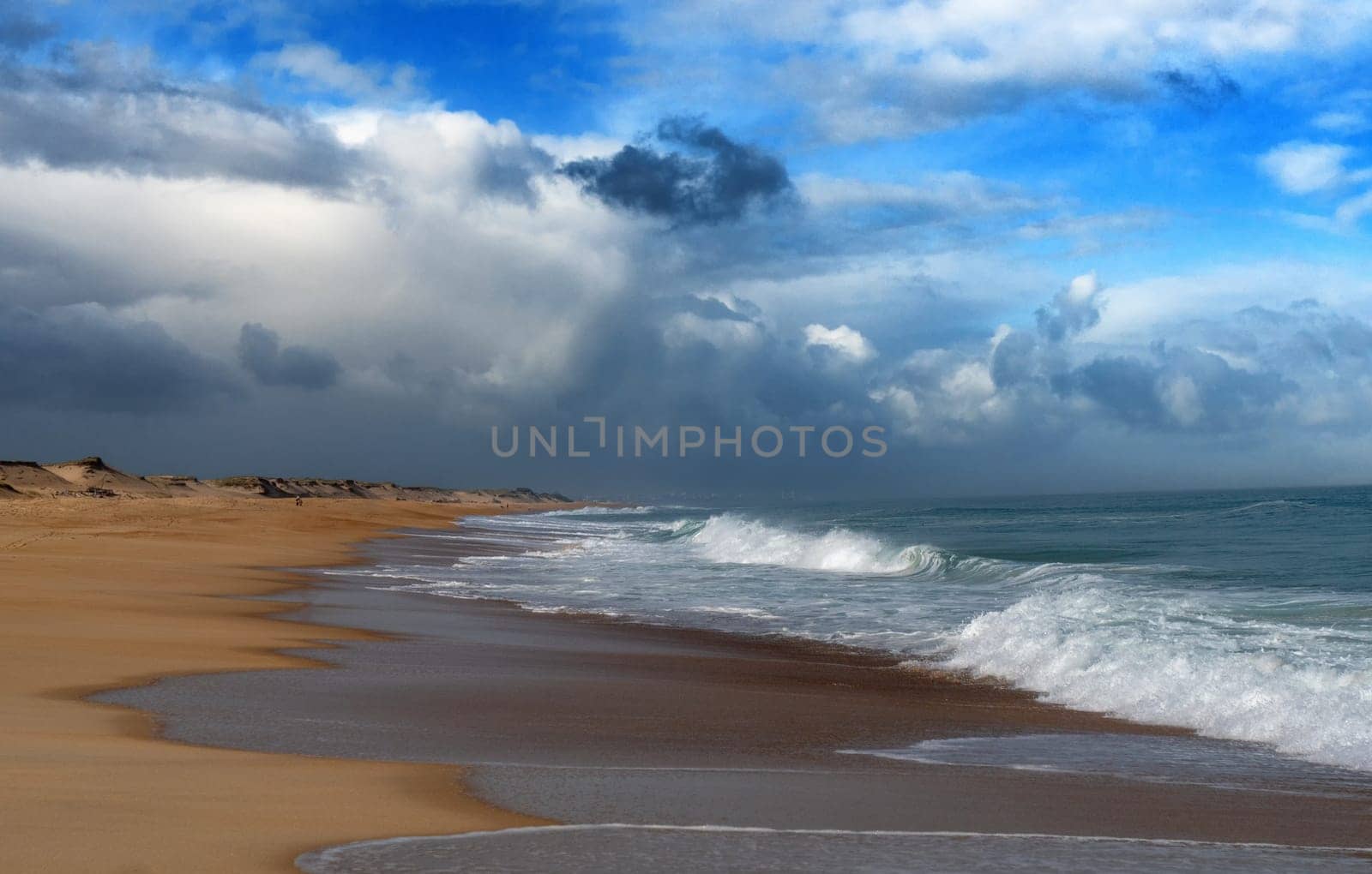 A beach with a cloudy sky in the background. The sky is mostly cloudy with some white clouds. The ocean is calm and the waves are small
