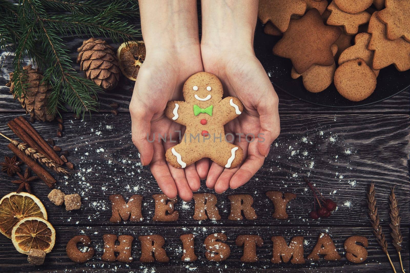Top view of woman hands holds gingerbread cookies on wood table with pine cones. New Year holiday and Christmas concept.