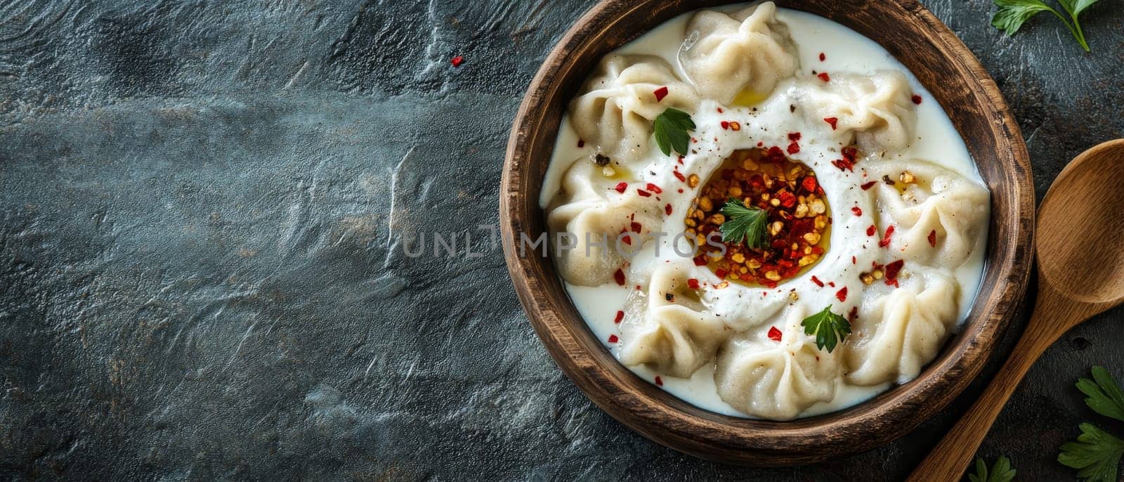 Traditional Georgian khinkali dumplings served in a creamy yogurt sauce with red chili oil and herbs in a rustic wooden bowl.