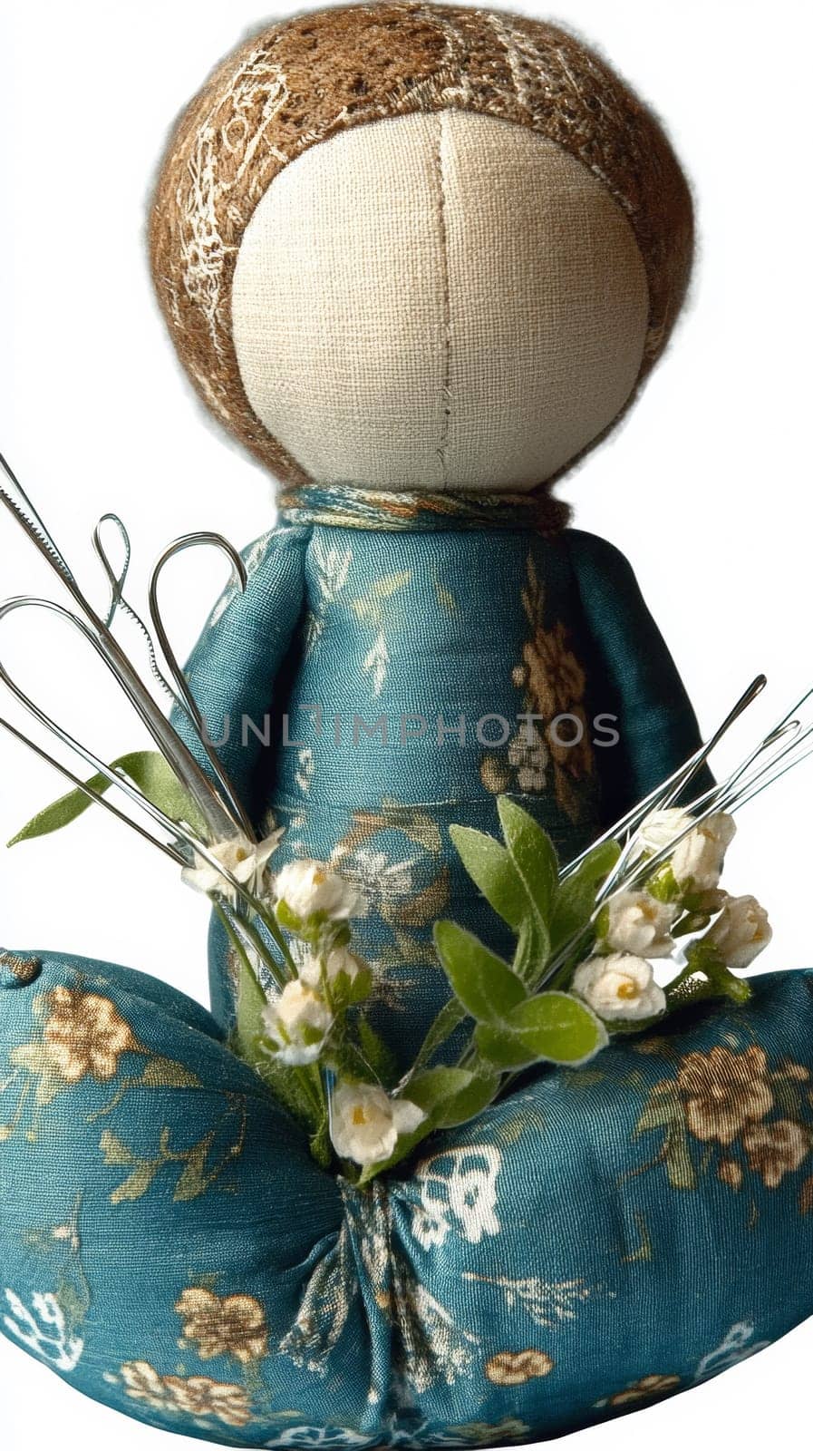 Handmade fabric pincushion doll in blue floral dress, accessorized with metal tools and small white flowers, creating an adorable craft atmosphere.