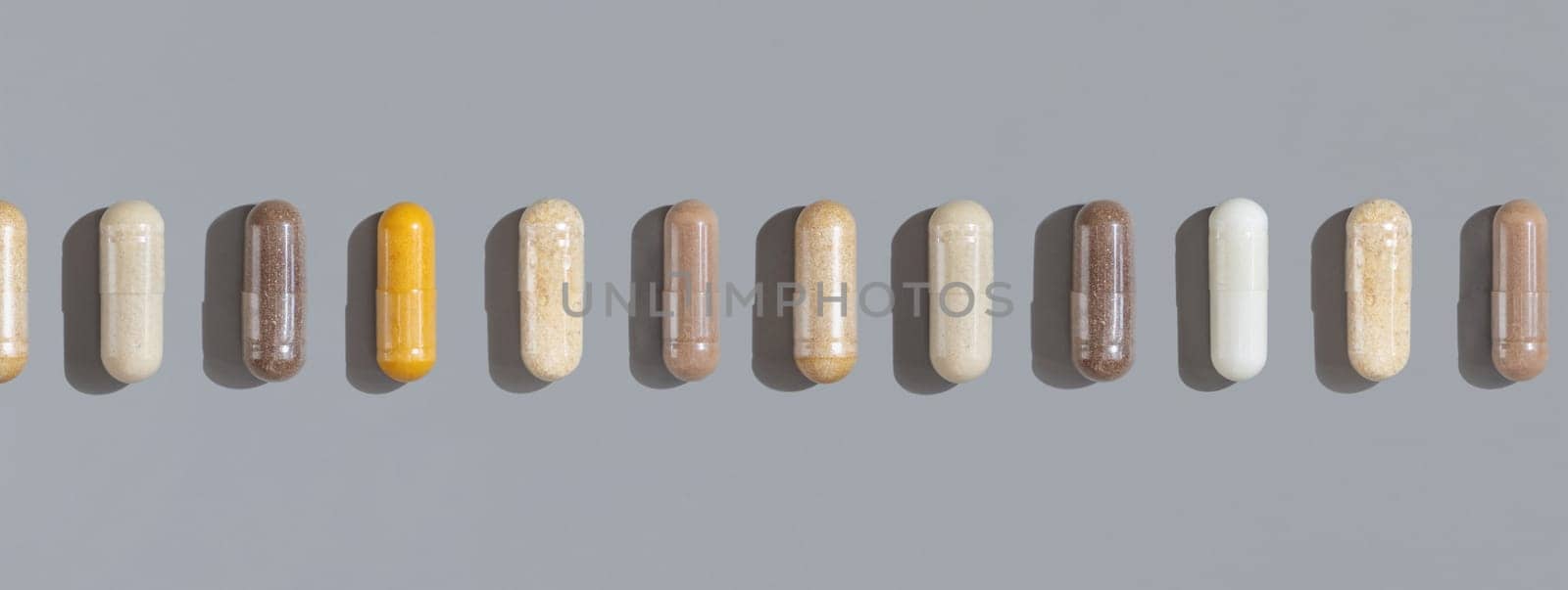 Mix of beige and brown medical capsules with one yellow in a line on grey top view, hard shadows. Preventive medicine and healthcare, herbal dietary supplements