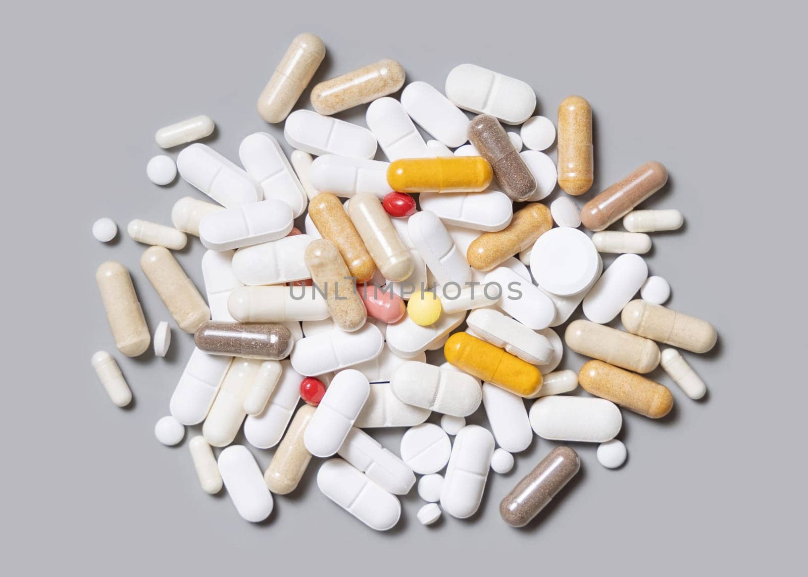 Mix of white, beige, red and yellow medical capsules and pills in a pile on grey top view. Medicinal treatment. Taking dietary supplements and vitamins. Assorted pharmaceutical products
