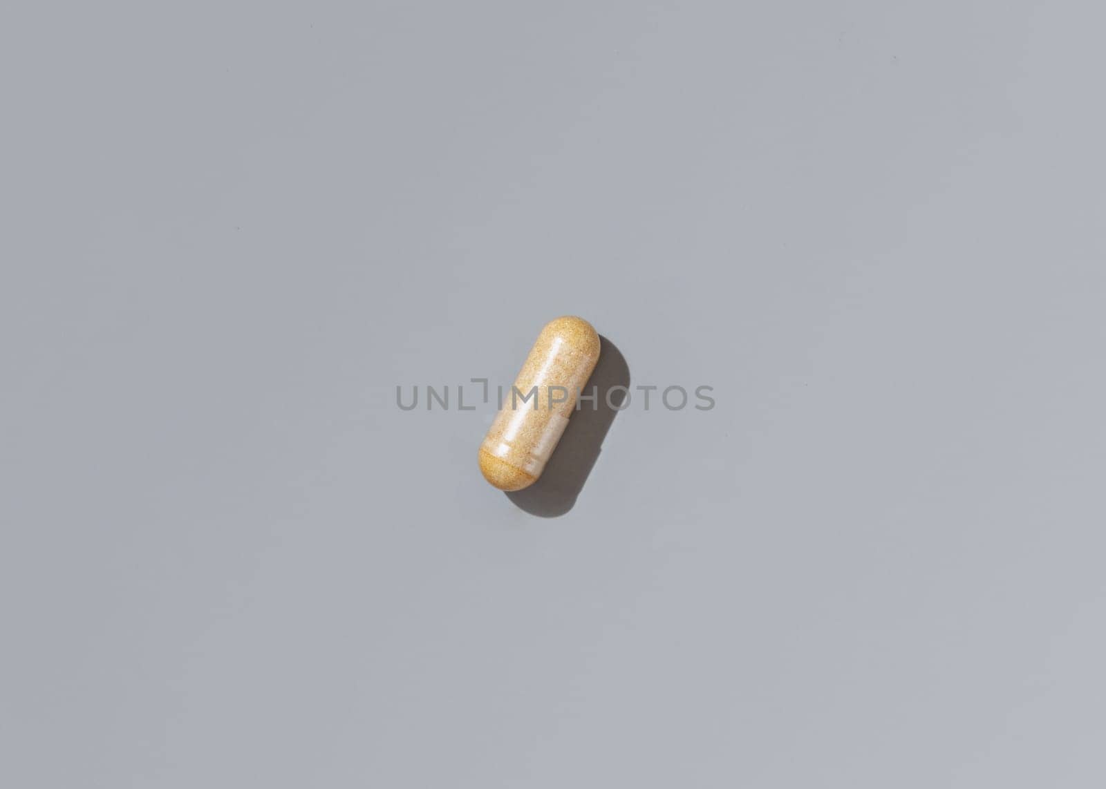 Yellow medical capsule on grey top view, hard shadows. Preventive medicine and healthcare, taking dietary supplements and vitamins. Minimal composition