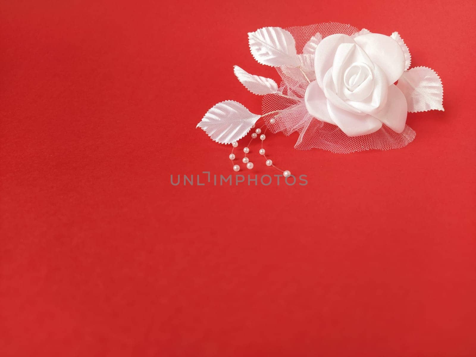 A stunning white rose stands out beautifully against a rich red background, complemented by soft leaves and small pearl accents, ideal for a wedding setting.
