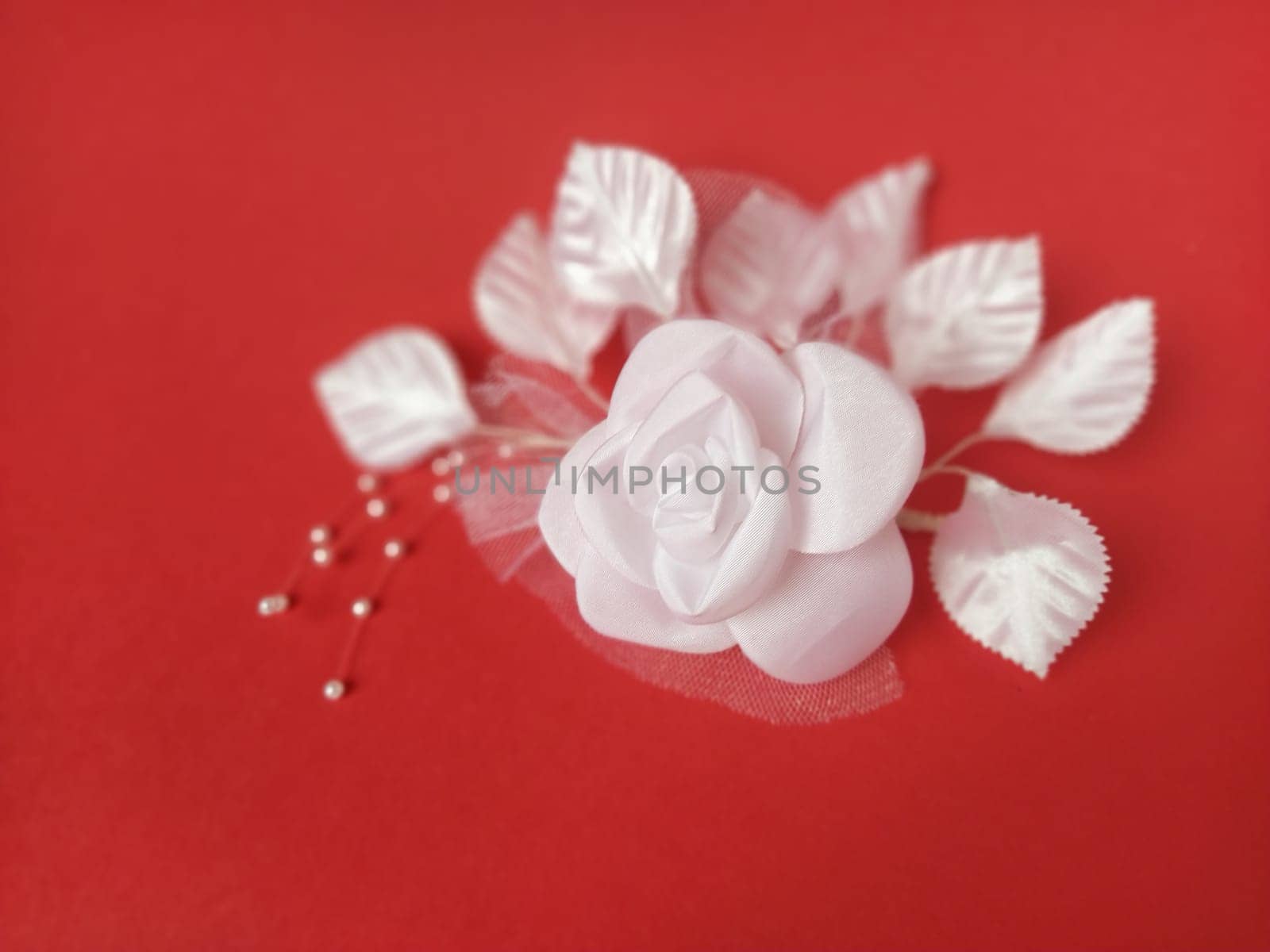 A stunning white rose stands out beautifully against a rich red background, complemented by soft leaves and small pearl accents, ideal for a wedding setting.